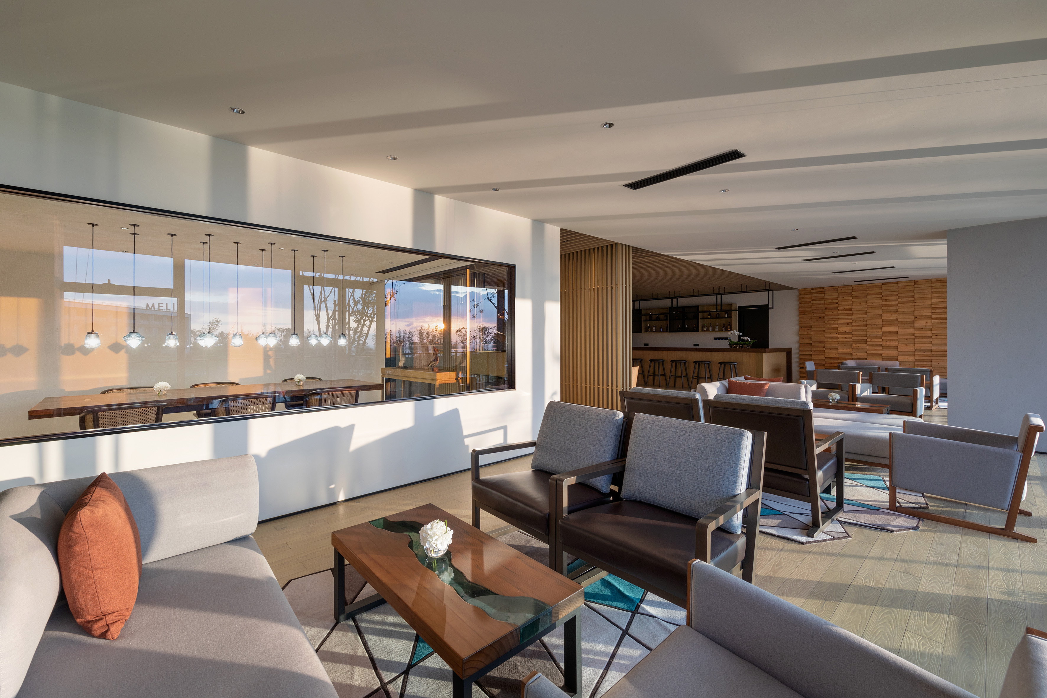 Modern hotel lounge with seating, bar, and sunset reflection on glass wall.