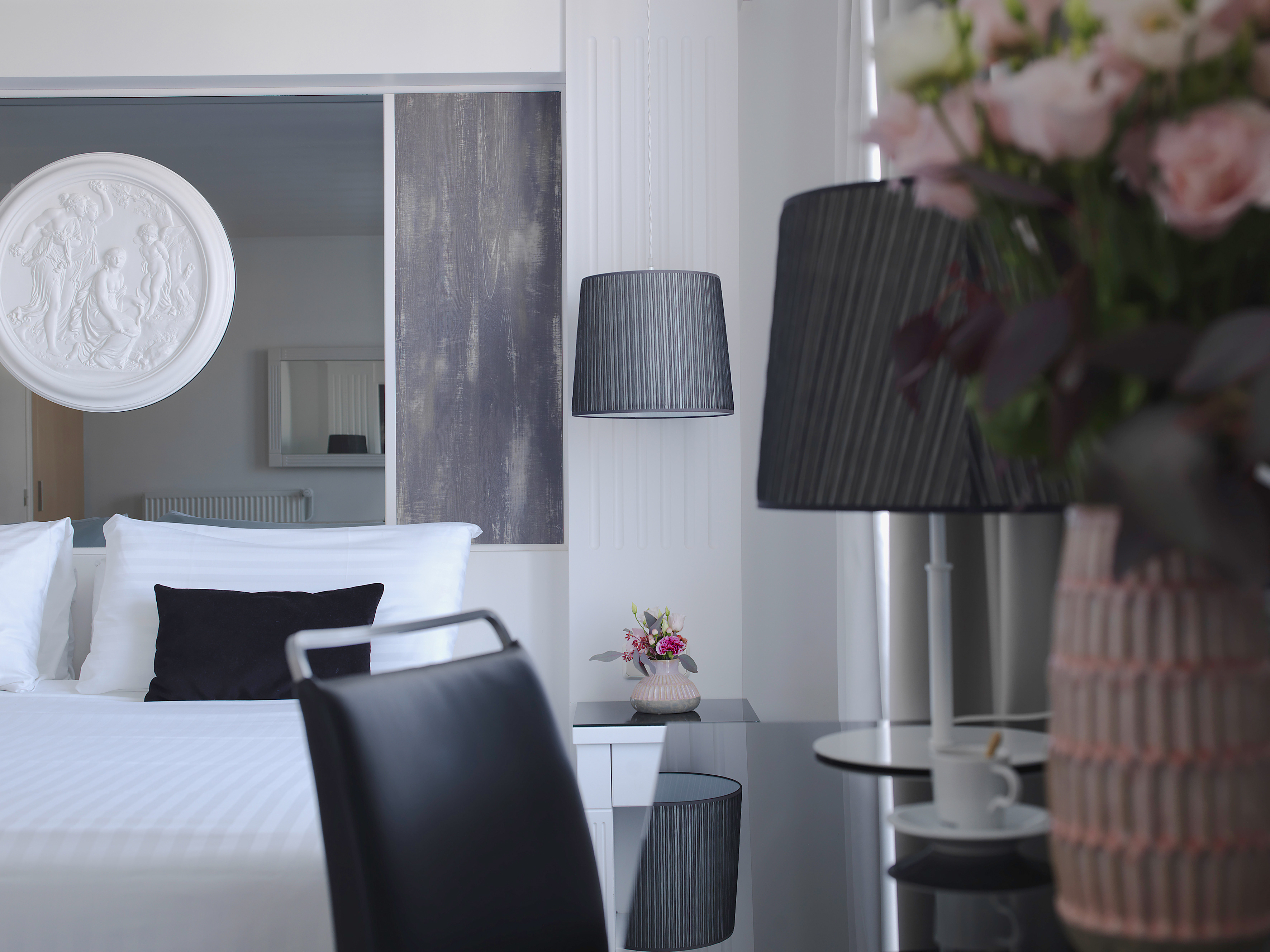 Modern hotel suite with bed, black pillow, lamps, pink flowers, and wall decor.