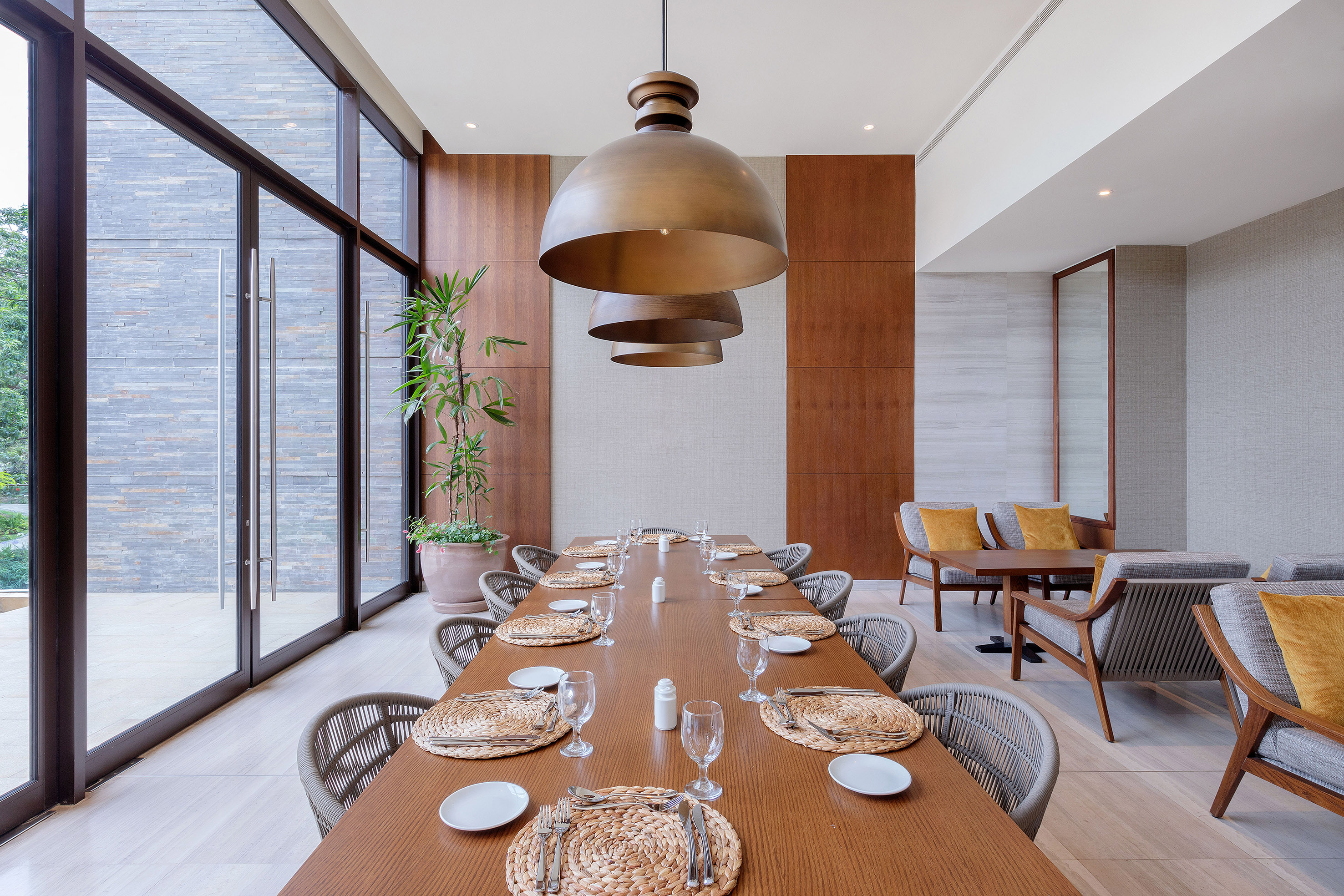 Modern dining room with long wooden table, large windows, and bronze pendant lights.