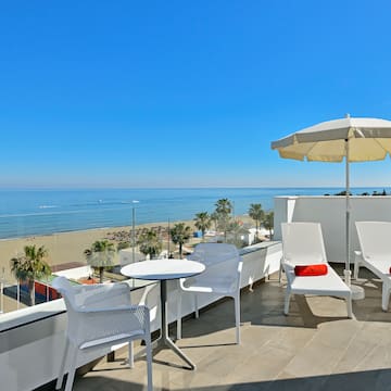 a white chairs and umbrella on a balcony overlooking a beach