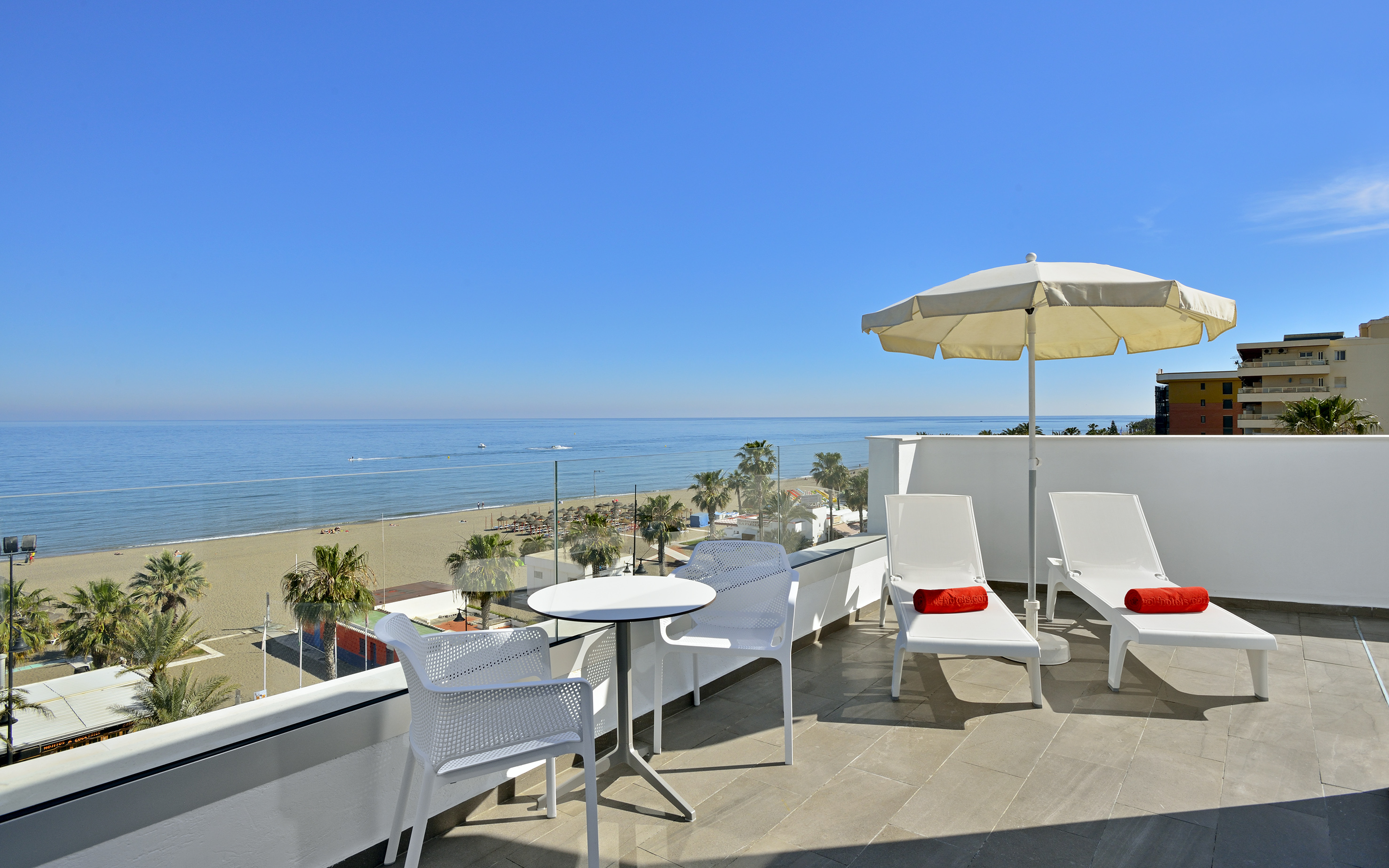 Beachfront balcony with sea view, lounge chairs, and palm trees.