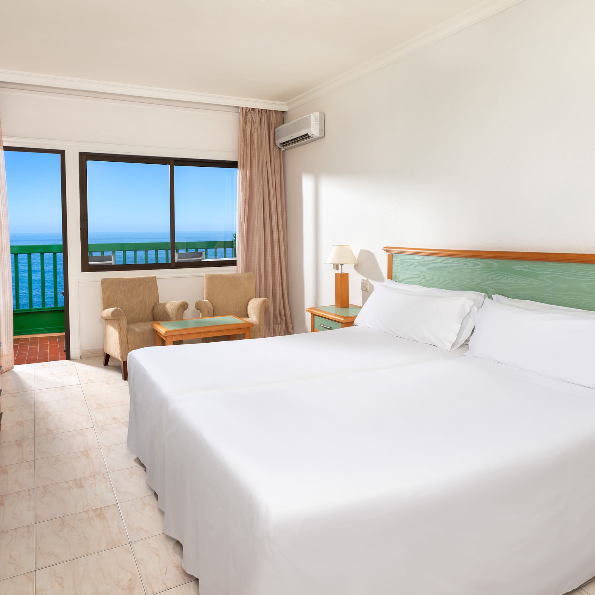 a room with a bed and a chair and a balcony overlooking the ocean