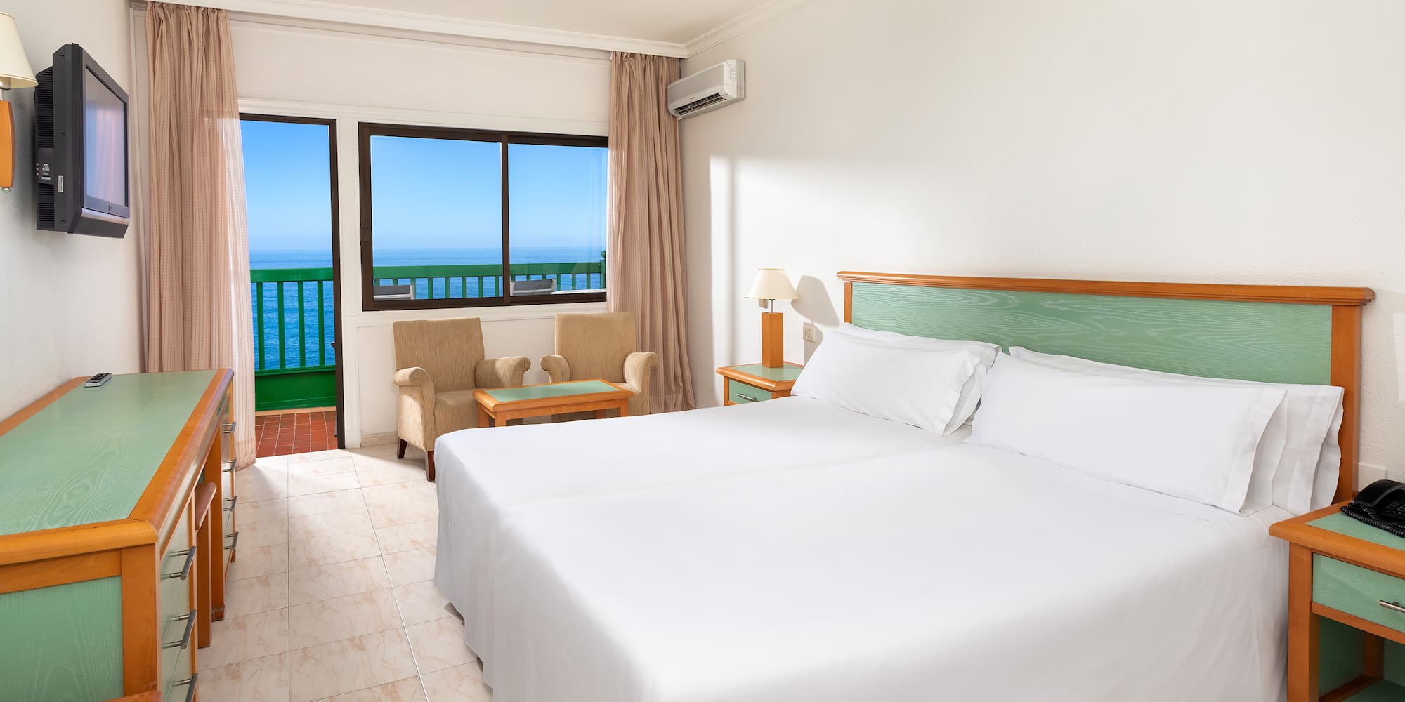 a room with a bed and a chair and a balcony overlooking the ocean