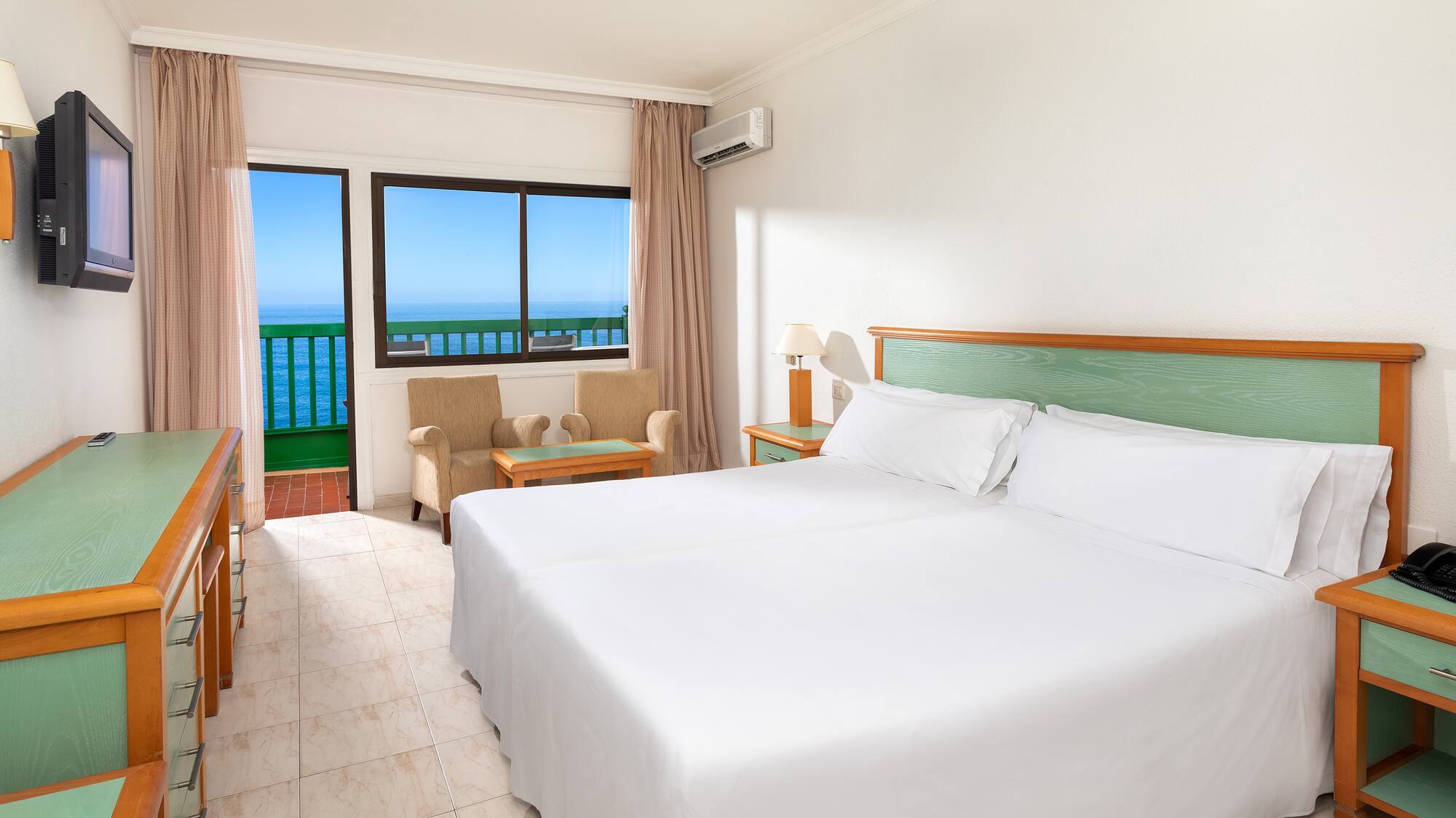 a room with a bed and a chair and a balcony overlooking the ocean