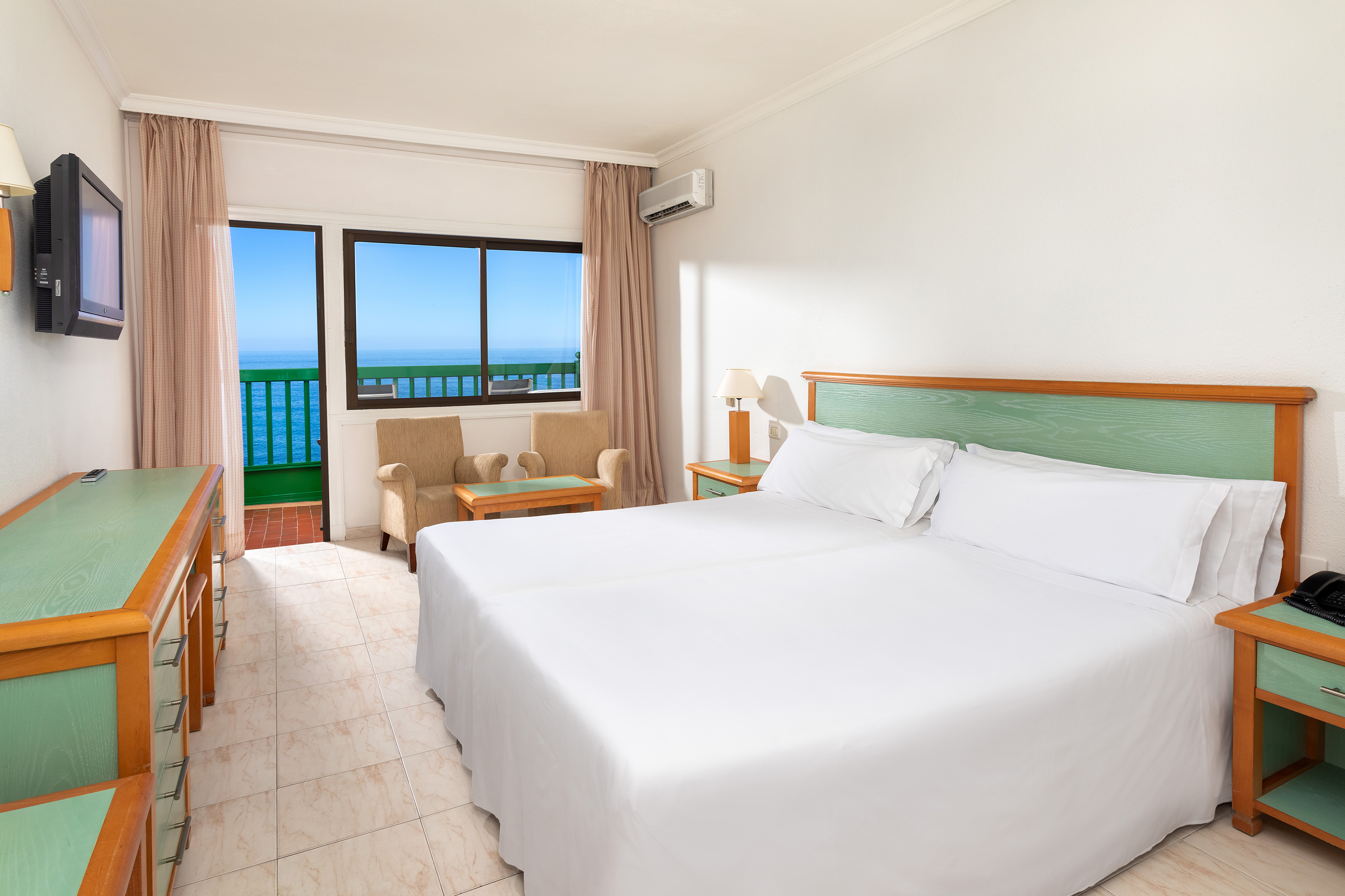Hotel room with ocean view, twin beds, balcony, green furniture accents.