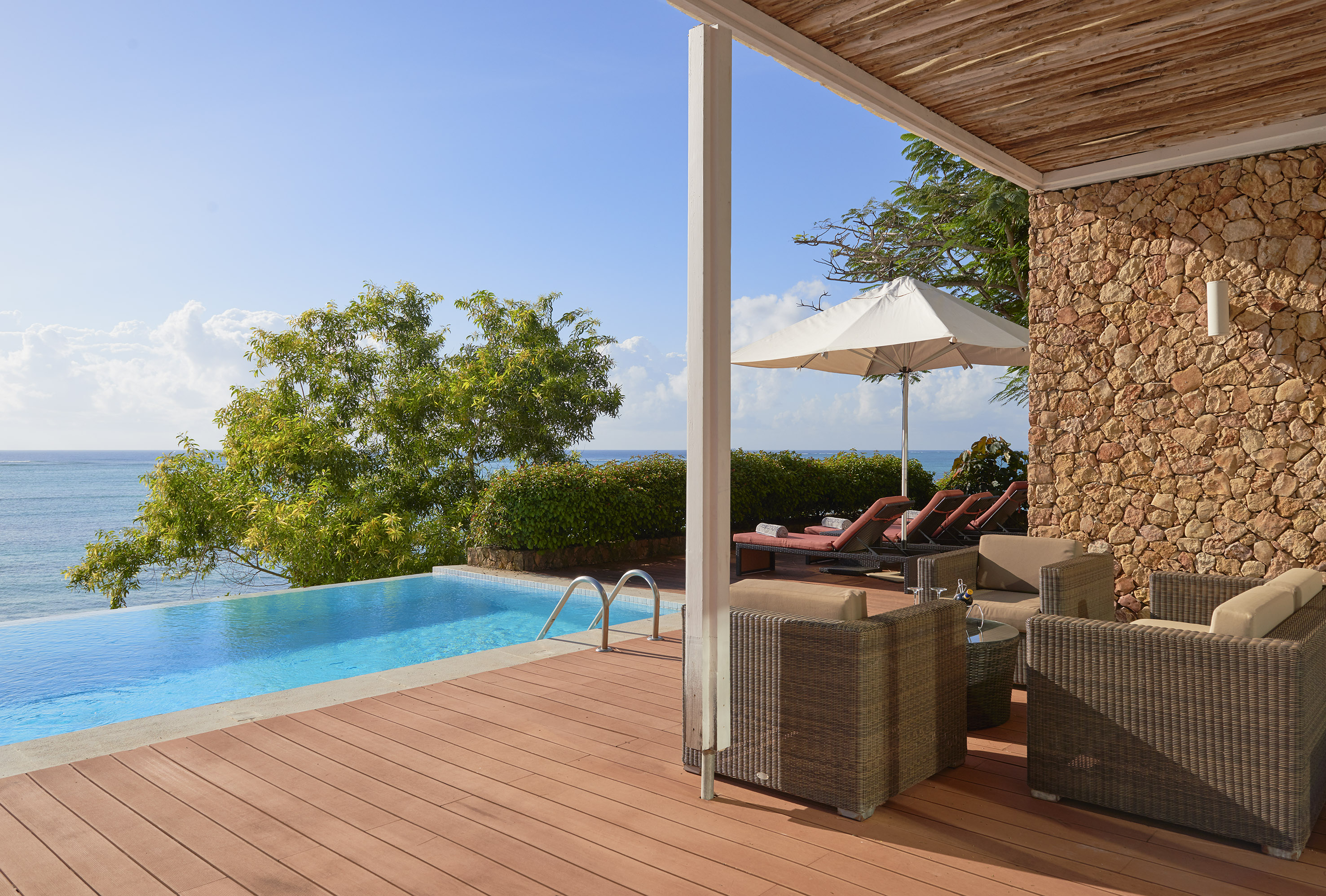 Luxury villa patio with ocean view infinity pool, wooden deck, and outdoor lounge.
