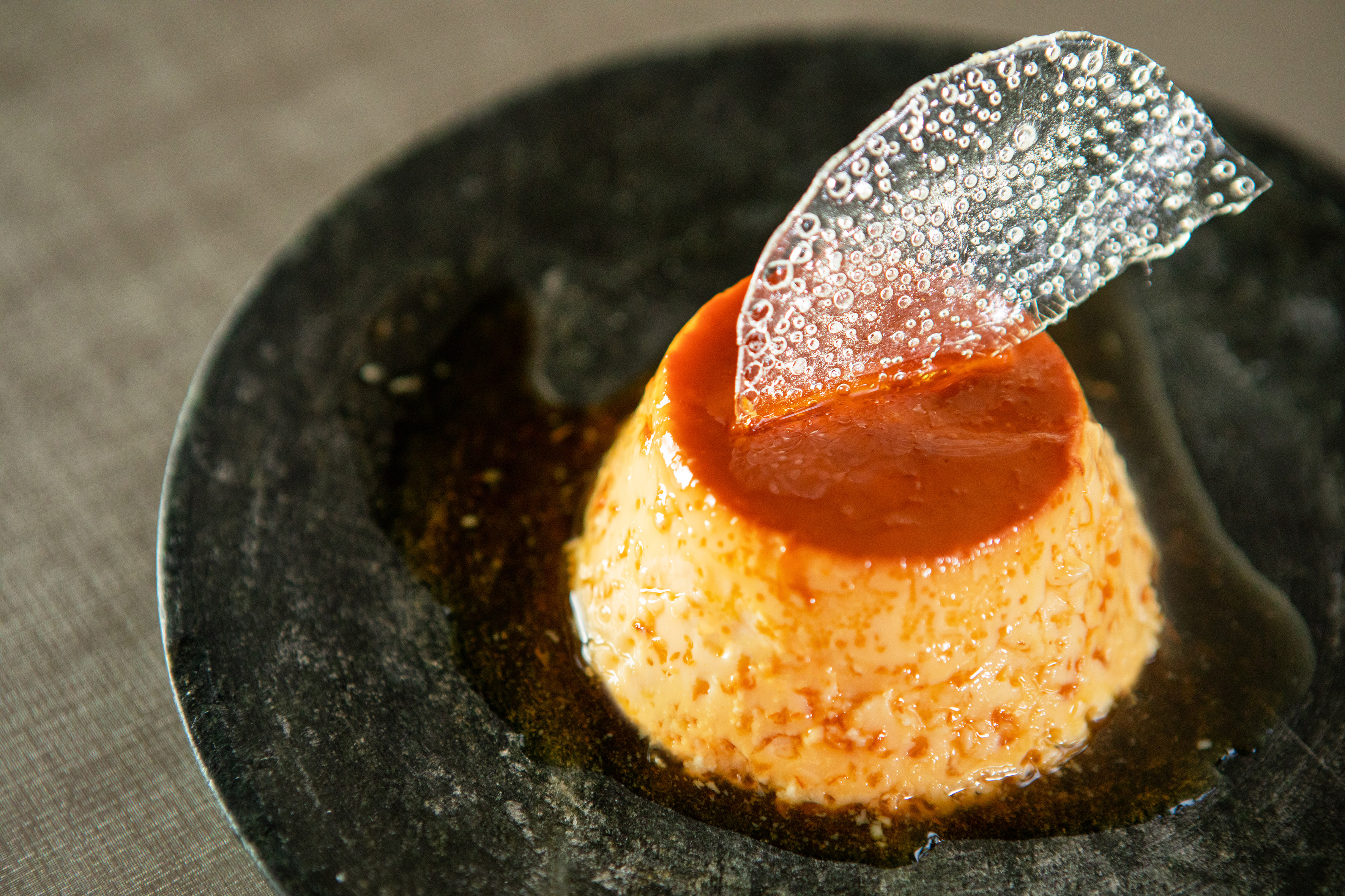Creamy caramel flan with glossy sauce and decorative sugar shard.