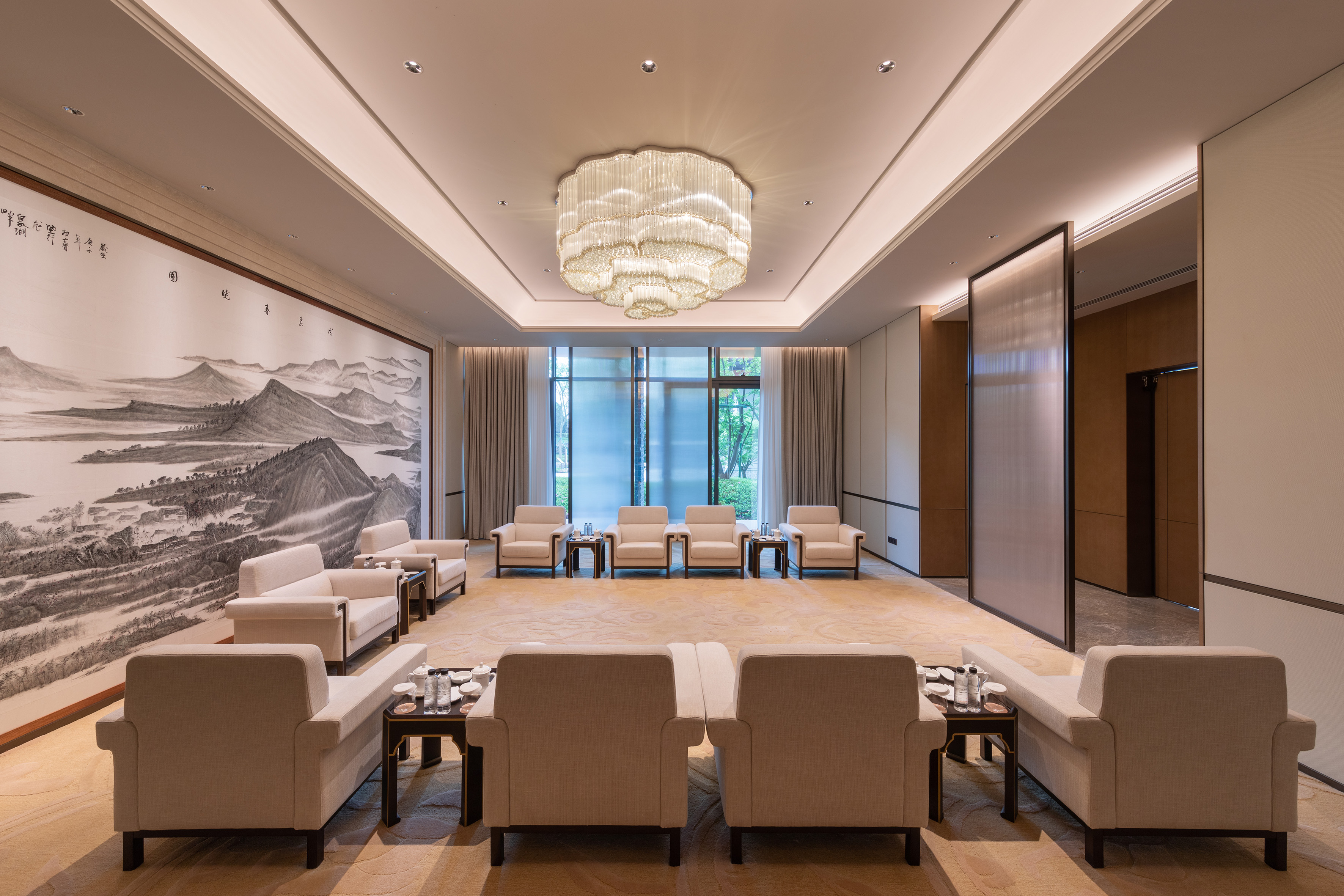 Elegant meeting lounge with modern sofas, crystal chandelier, and Chinese landscape art.