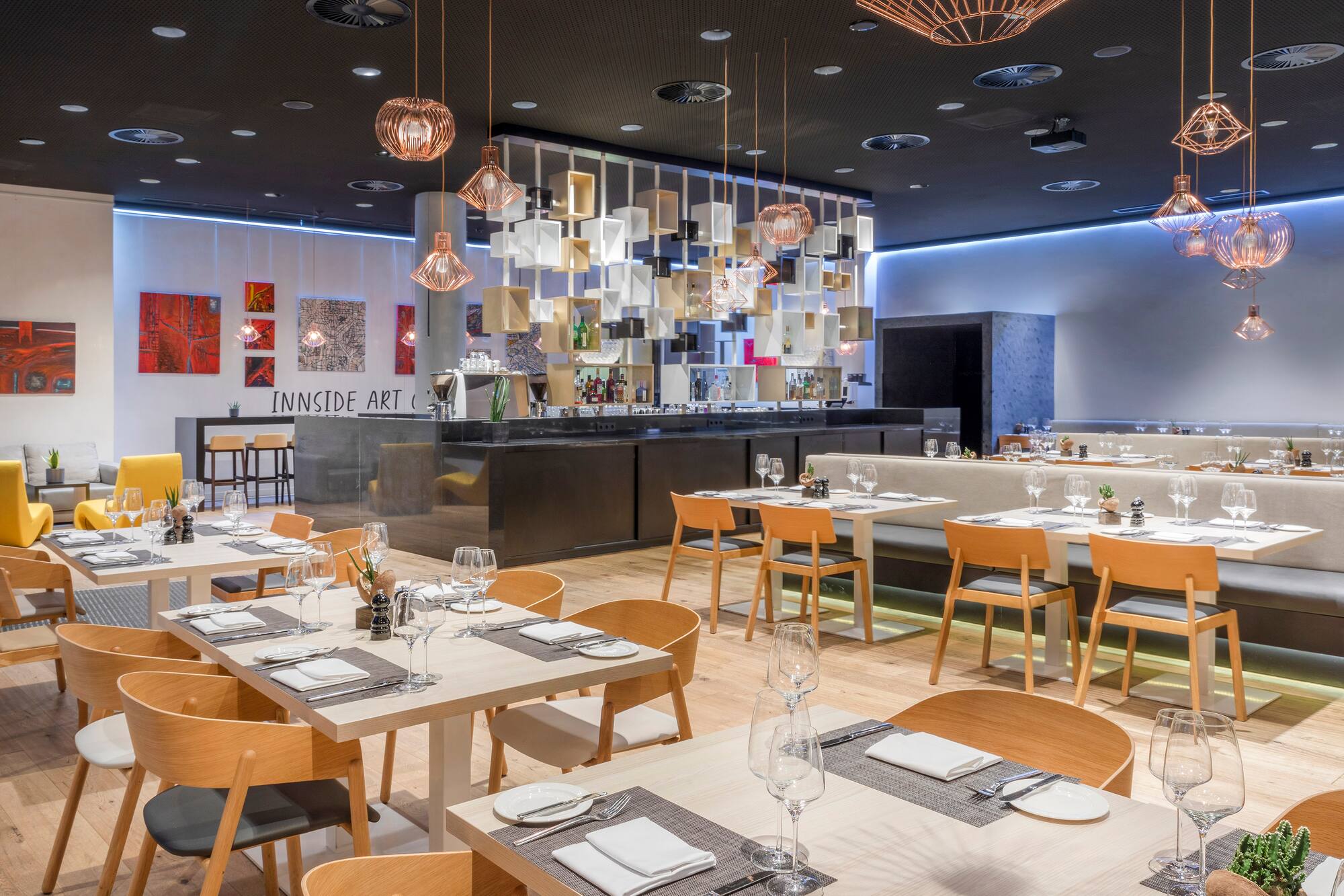 Contemporary restaurant with set tables, a modern bar, and artistic lighting.