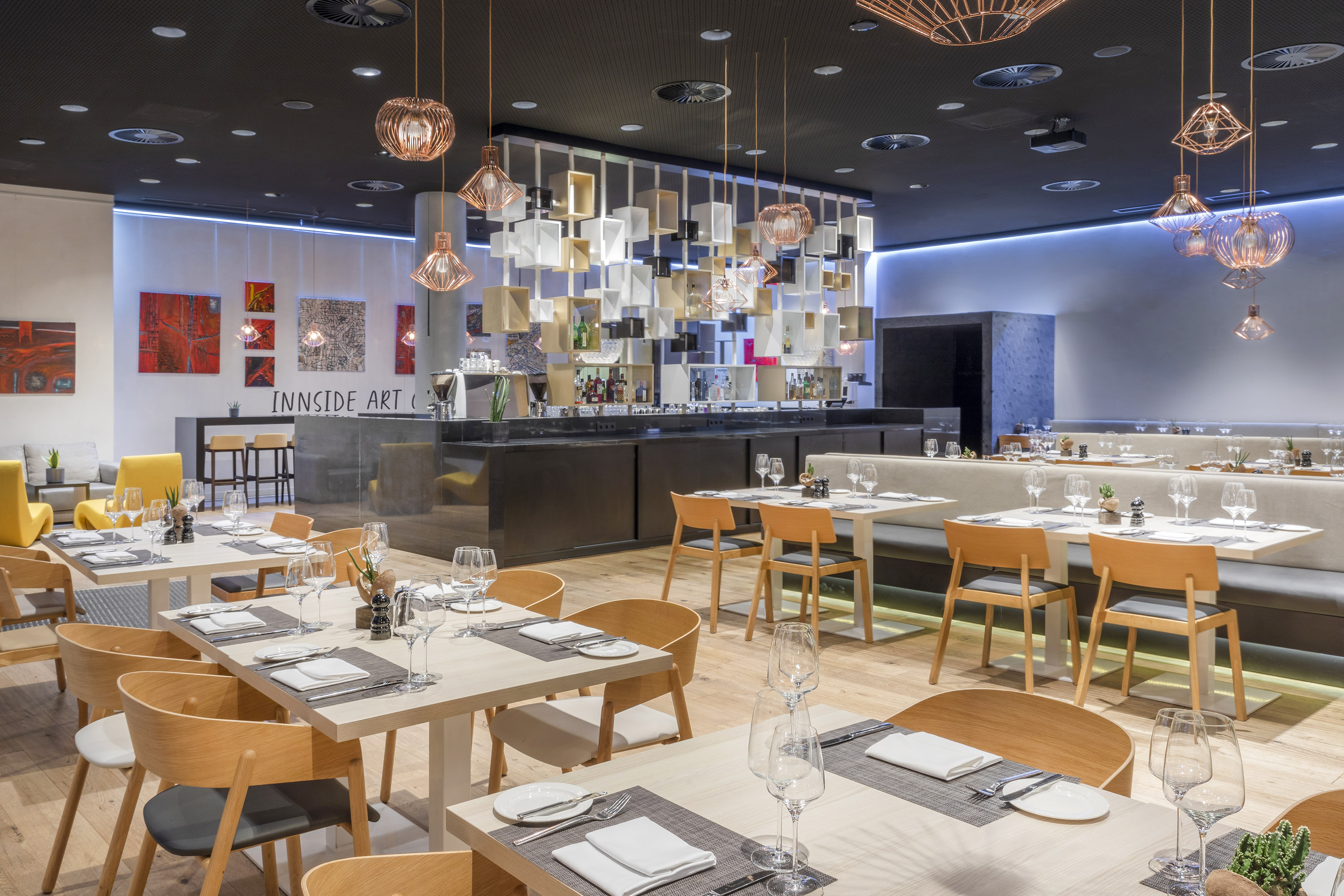 Contemporary restaurant with set tables, a modern bar, and artistic lighting.