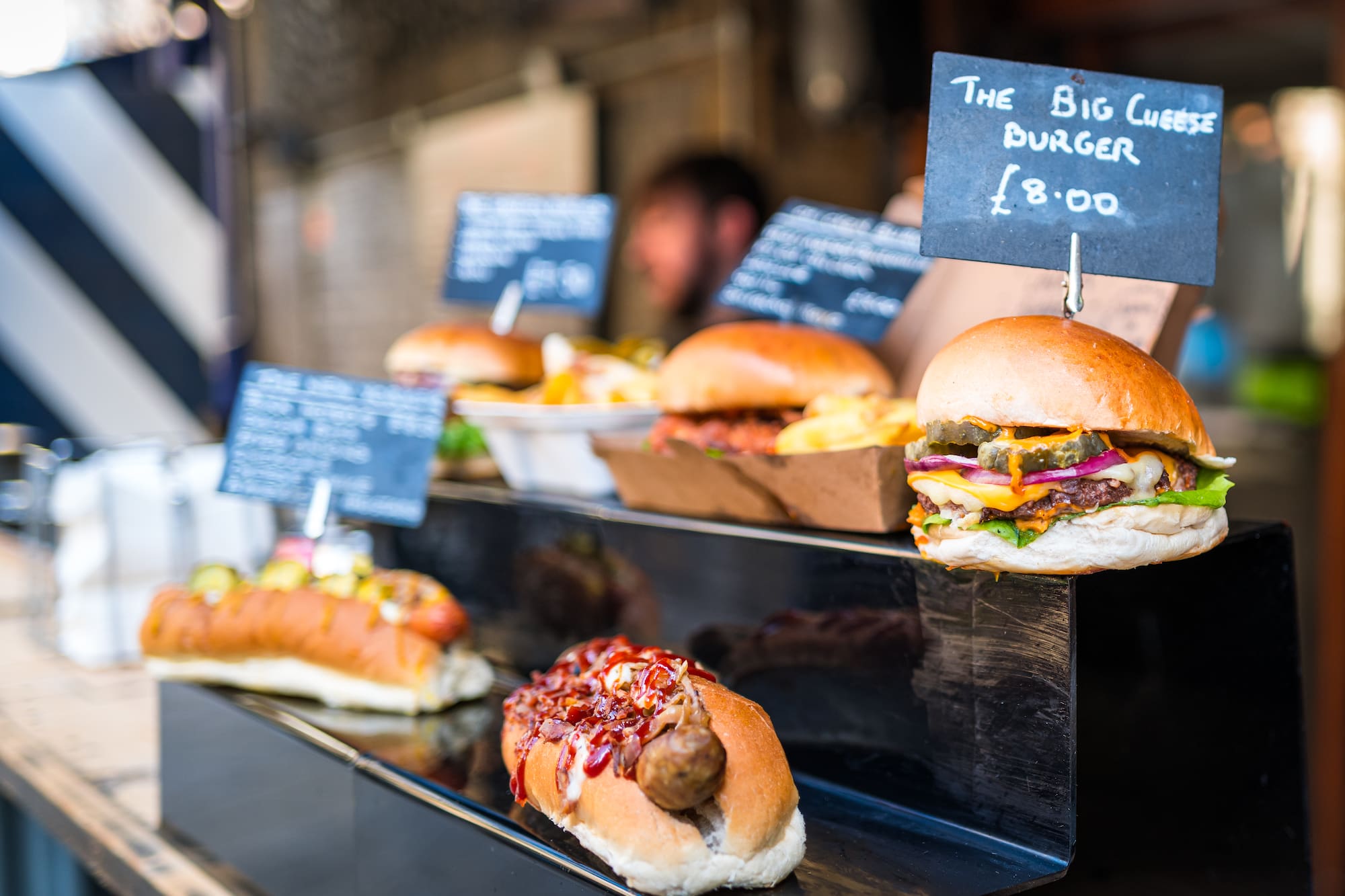 Street food stall with gourmet burgers, hot dogs, and fries, with "Big Cheese Burger" sign.