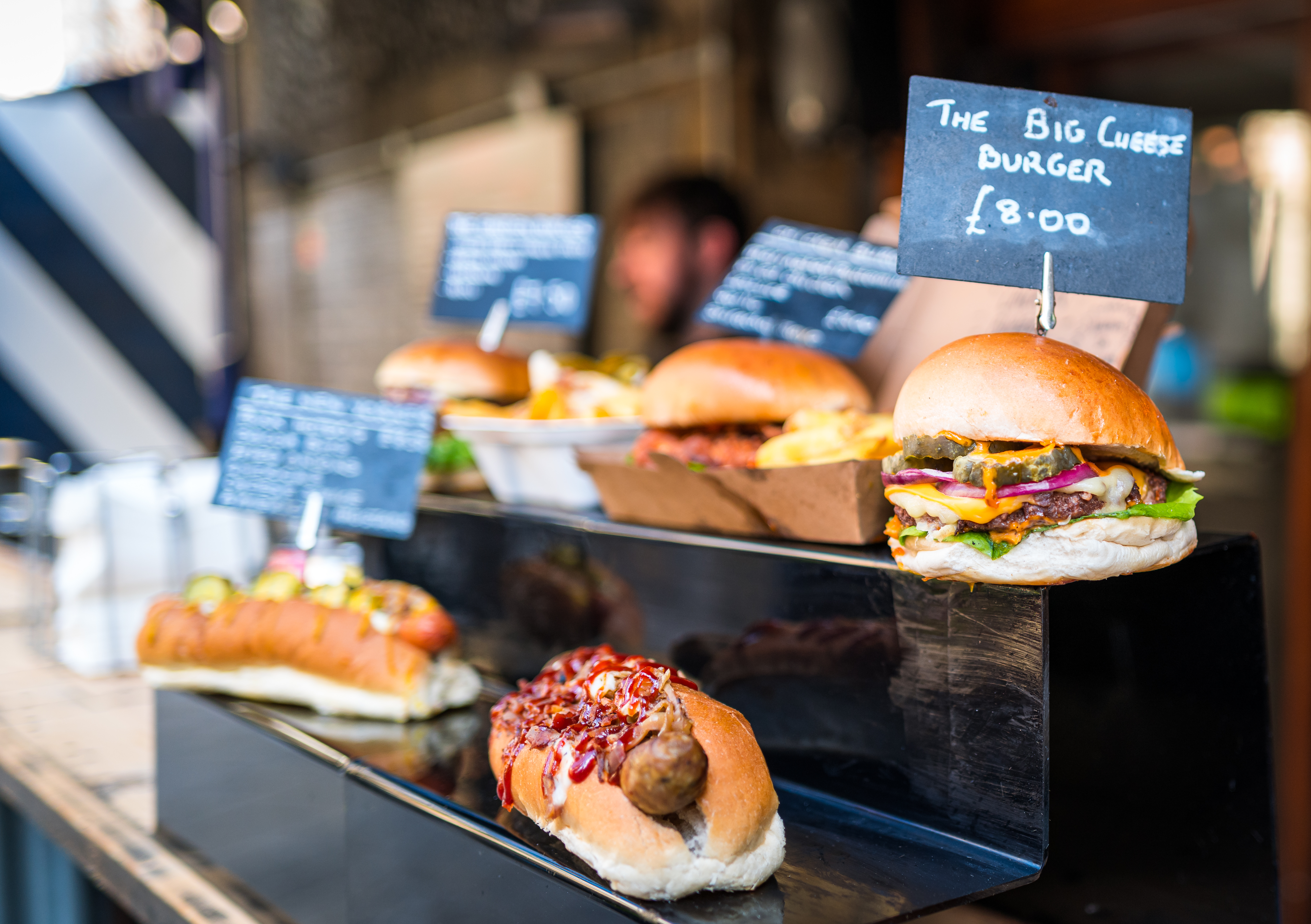 Street food stall with gourmet burgers, hot dogs, and fries, with "Big Cheese Burger" sign.