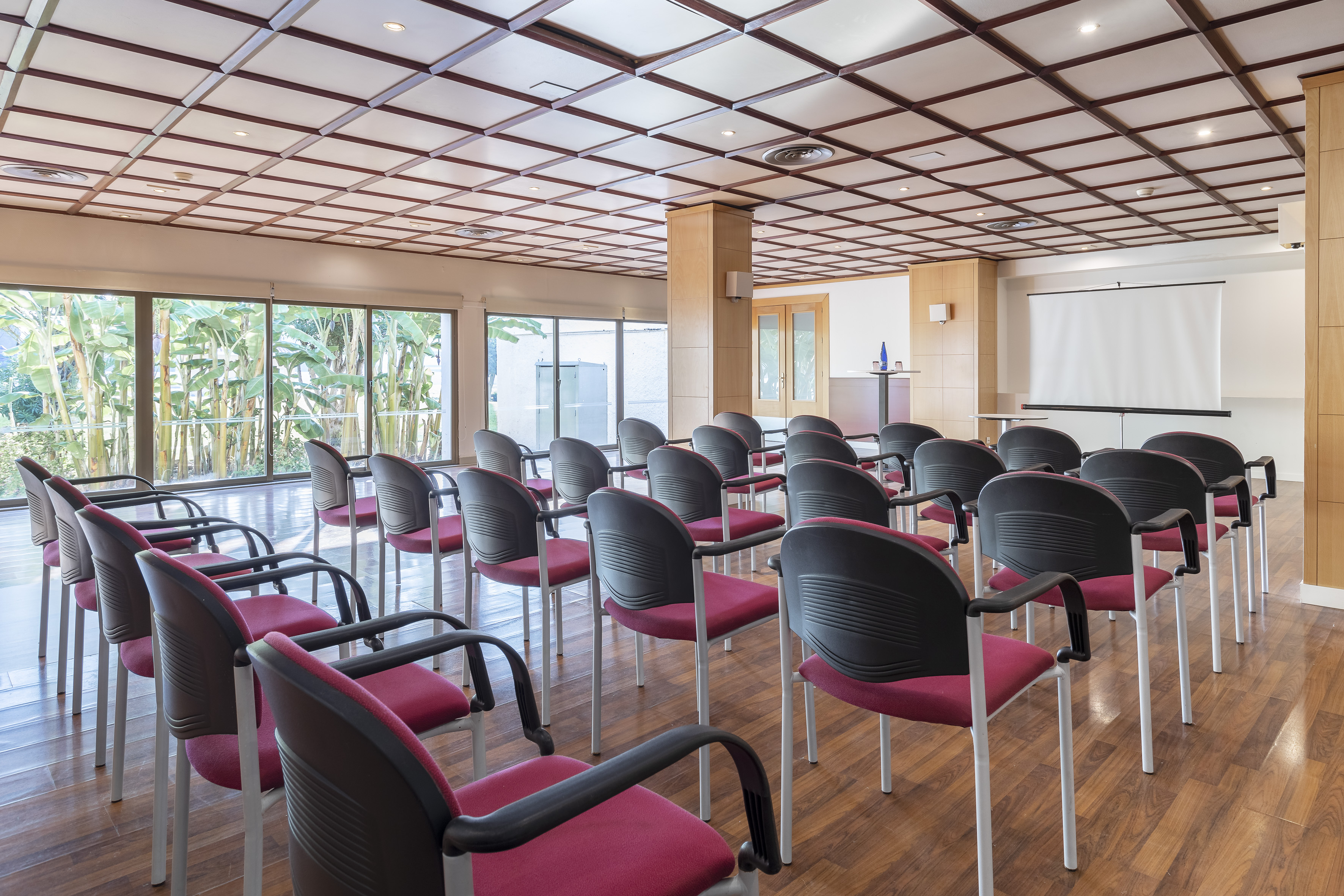 Empty meeting room with red chairs, projection screen, and large windows.