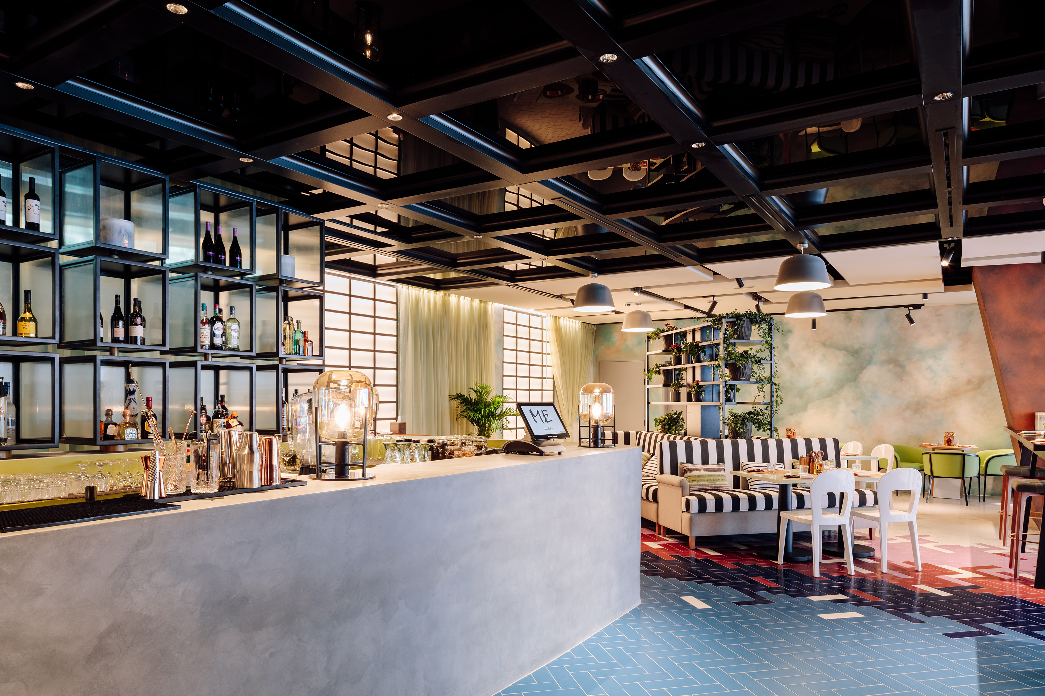 Modern bar and lounge with concrete counter, bottle display, and colorful tiled floor.