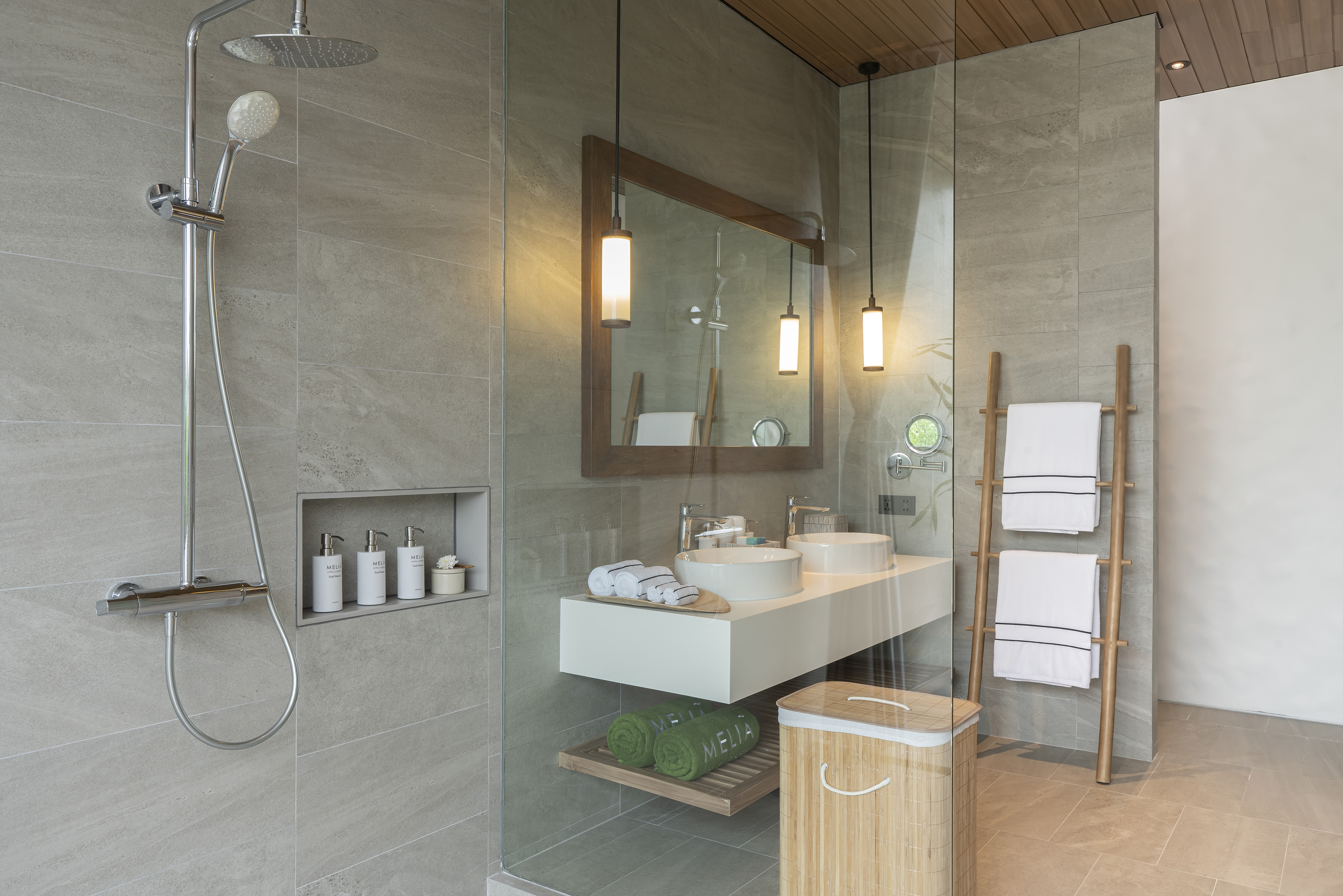 Modern bathroom with rain shower, dual vanity, wood mirror, and grey tiles.