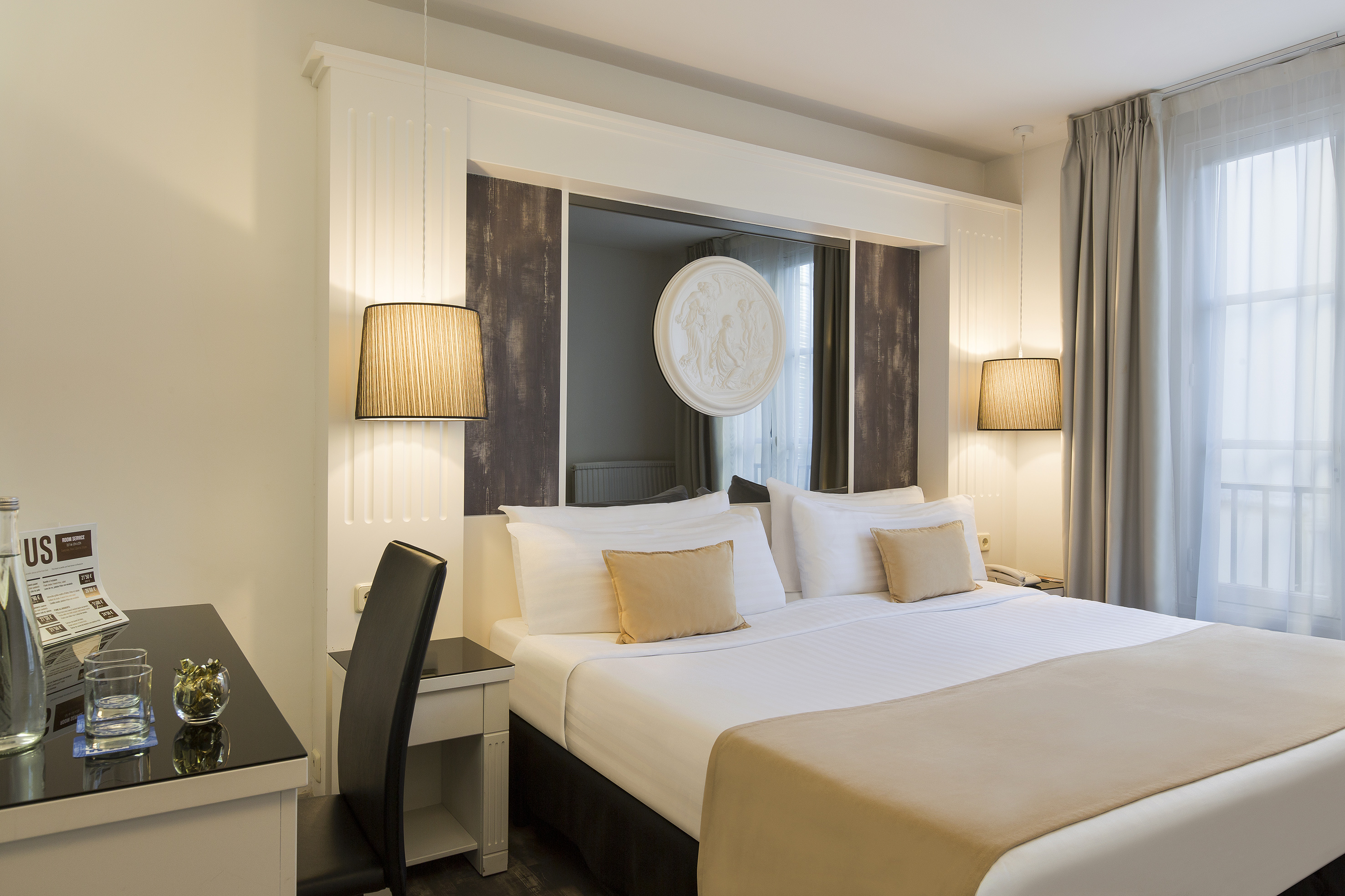 Modern hotel room with comfortable white bed, stylish headboard, desk, and warm lighting.