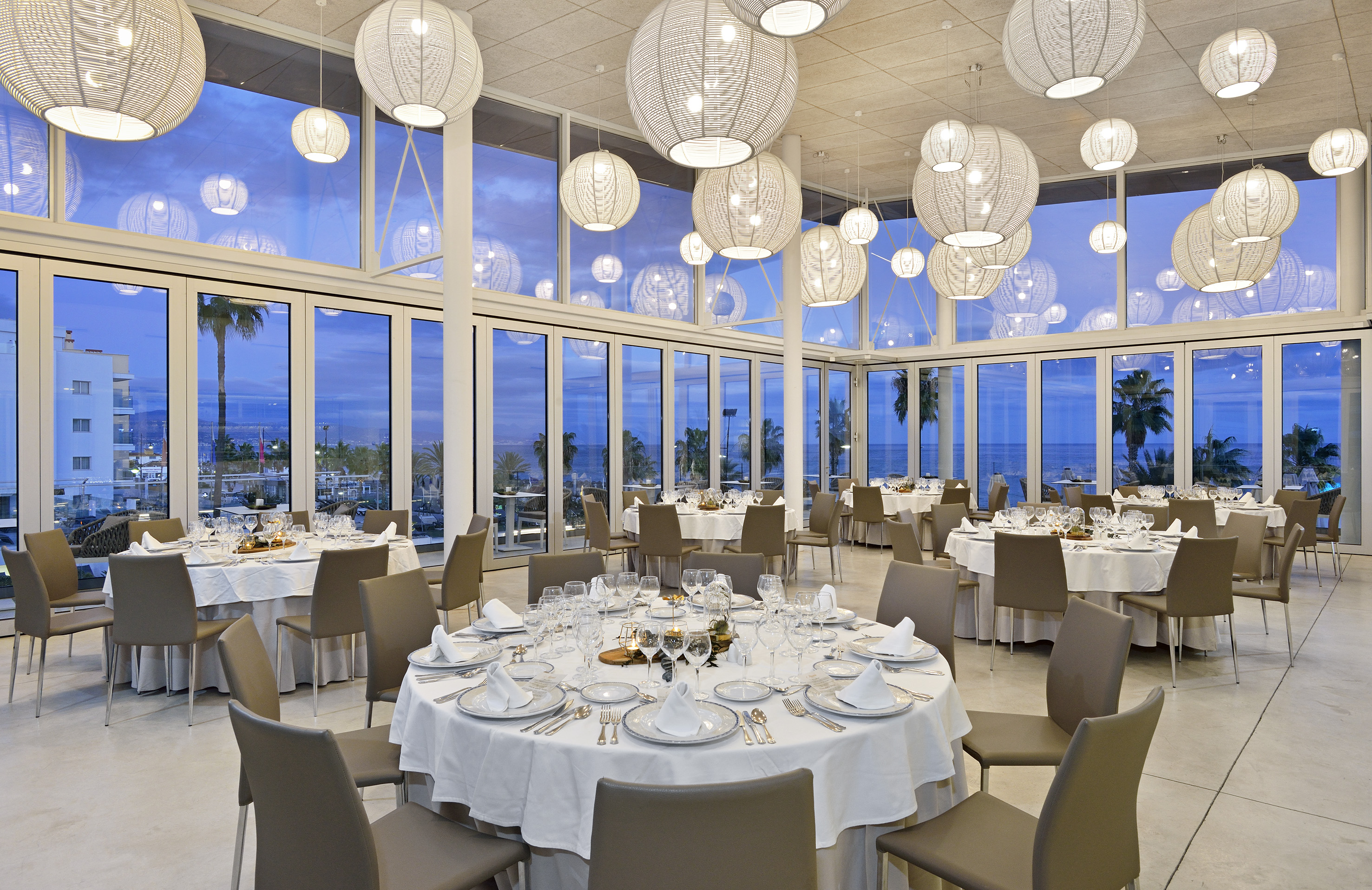 Elegant dining room with sea view, modern lighting, and fully set tables.