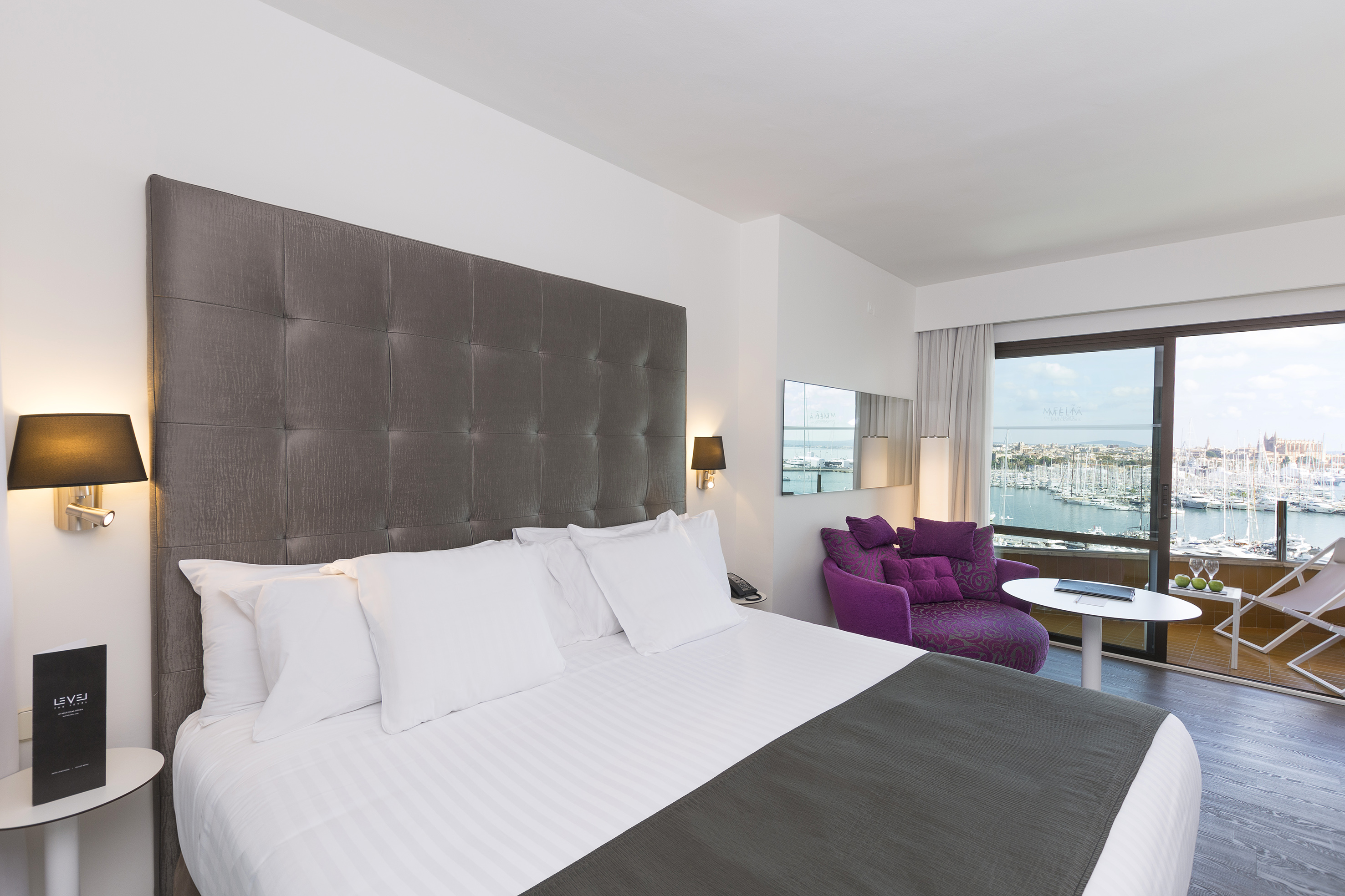 Luxury hotel bedroom with marina view and modern purple armchair.