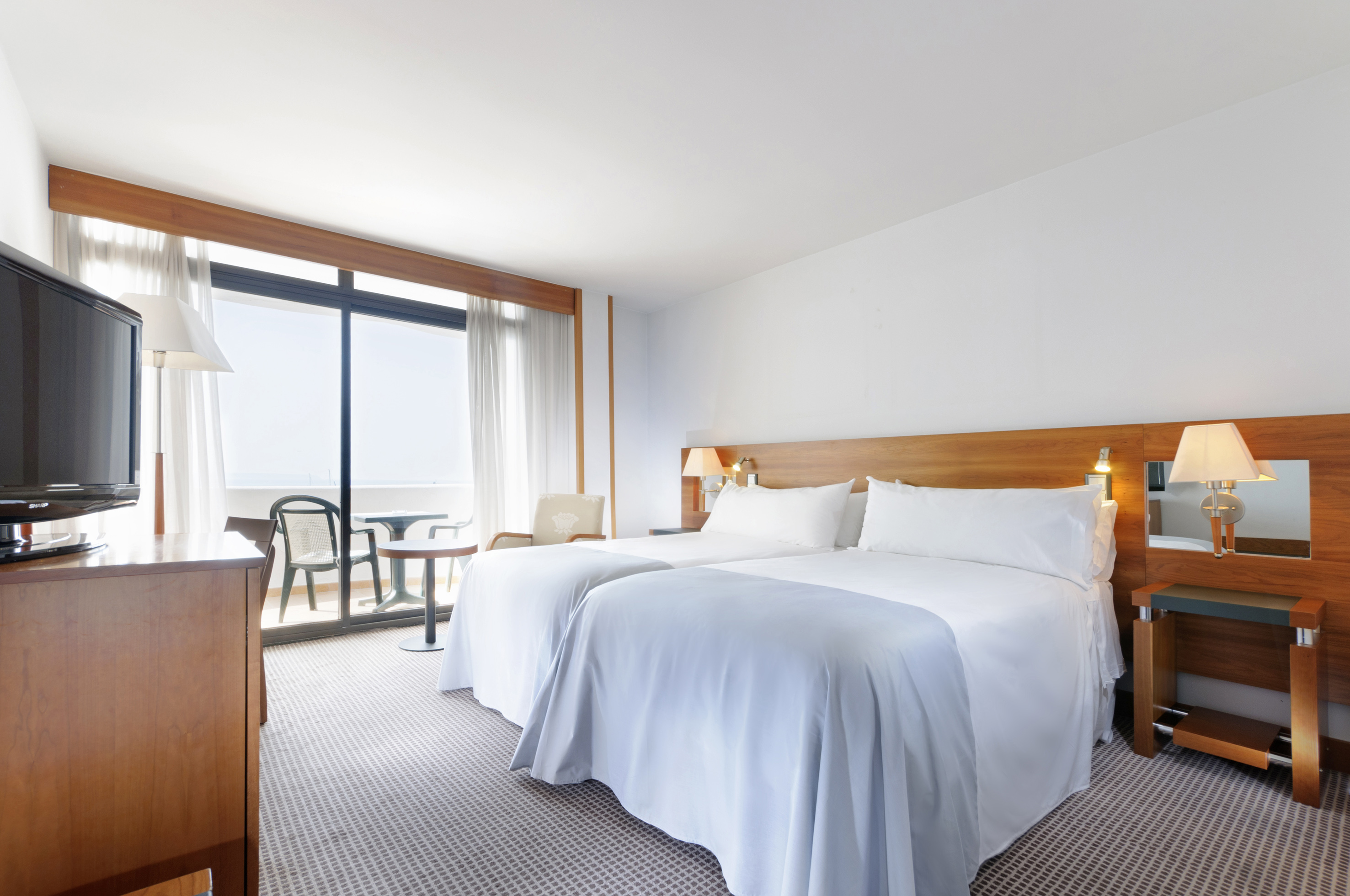 Hotel room with twin beds, private balcony, and distant sea view.
