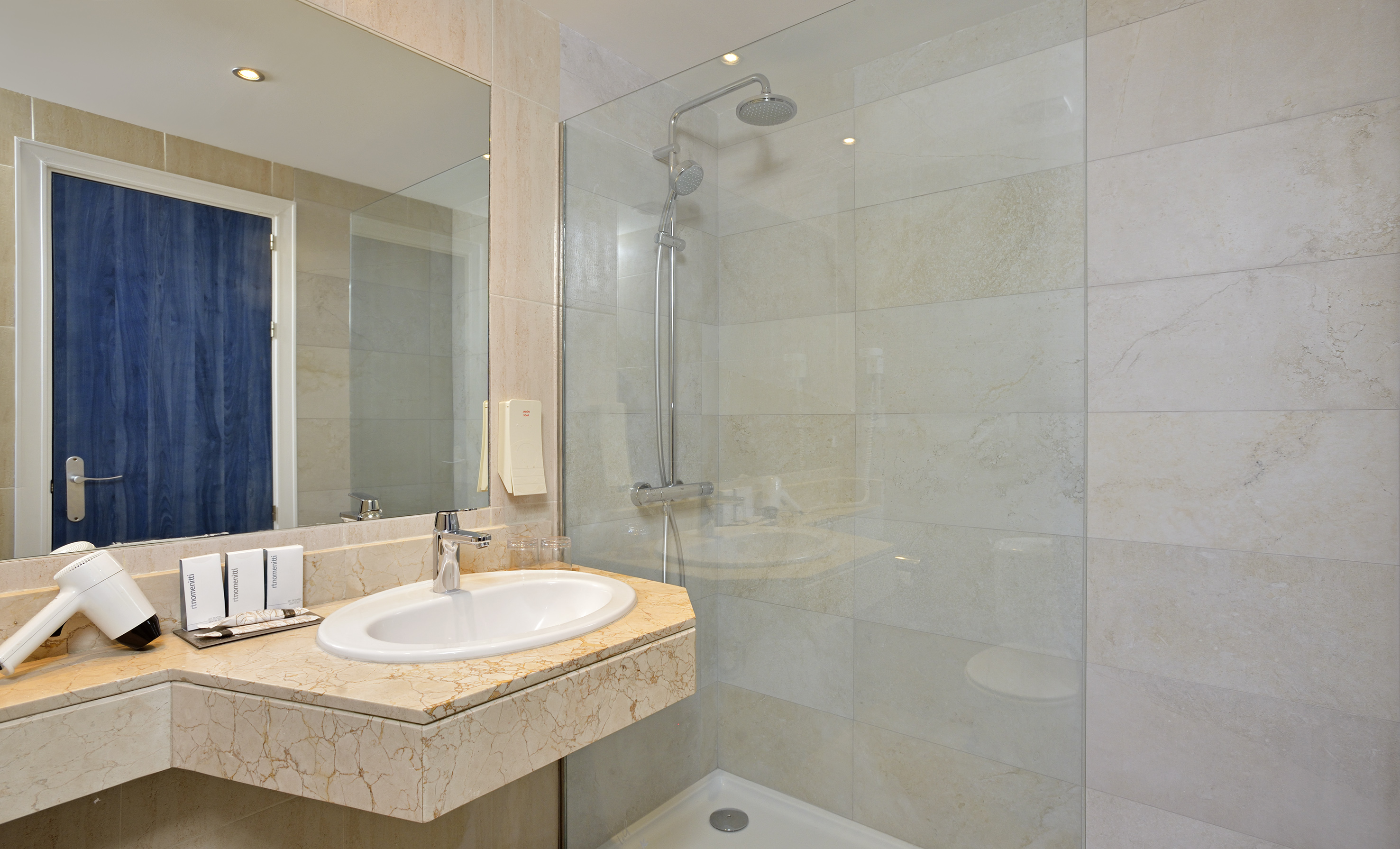 Modern hotel bathroom with marble vanity, white sink, mirror, and glass shower.