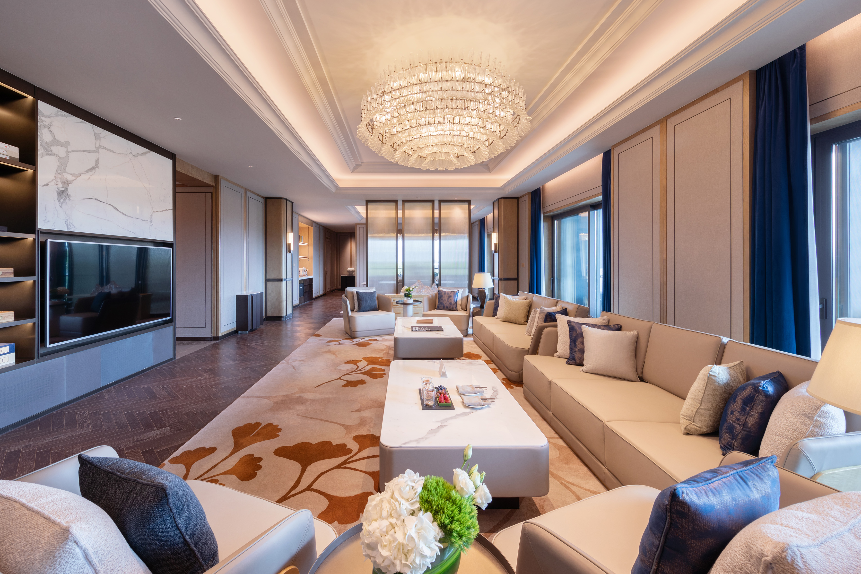 Luxury living room with beige sofas, marble tables, and crystal chandelier.