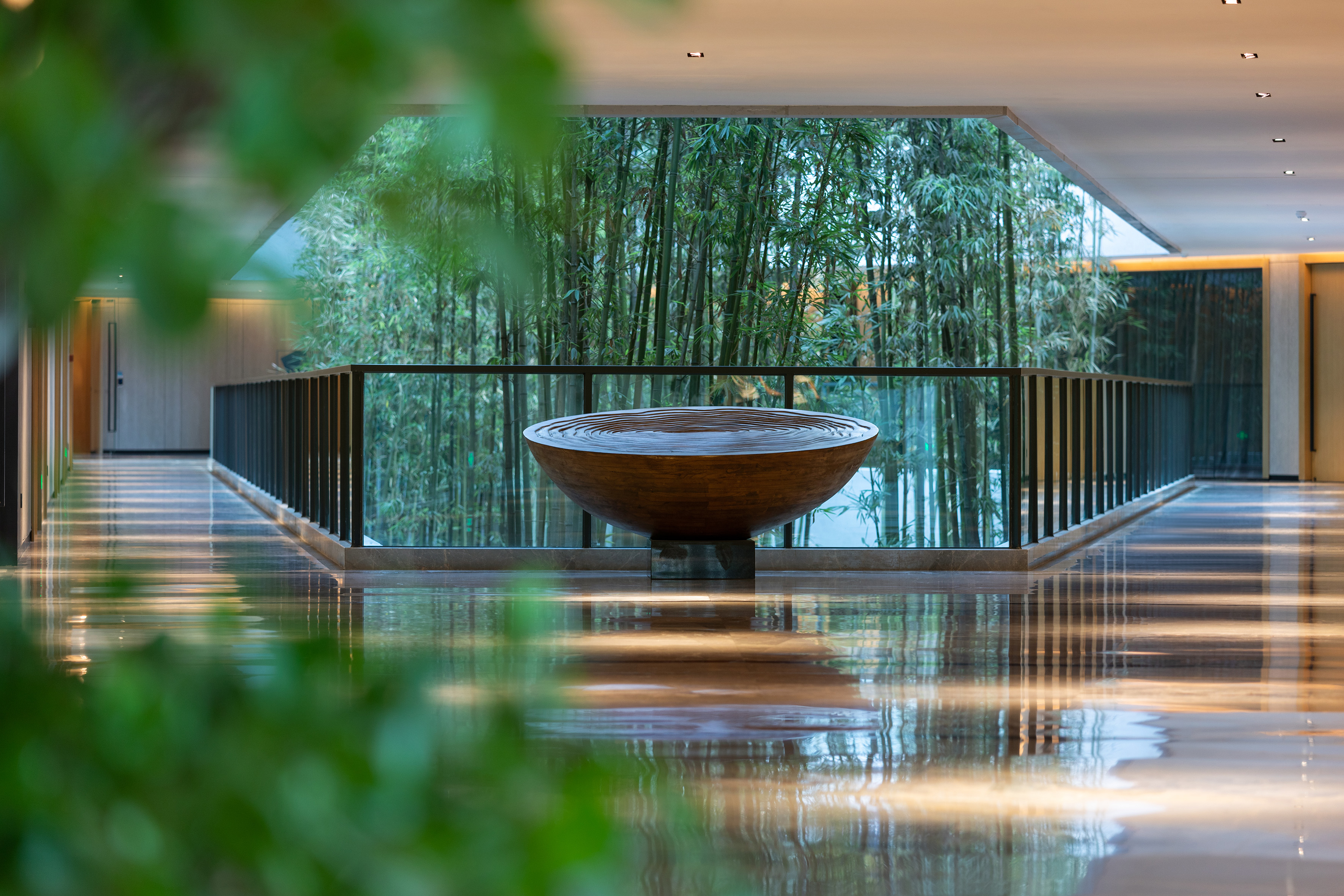 Modern lobby with reflective floor, circular water feature, and bamboo forest view.