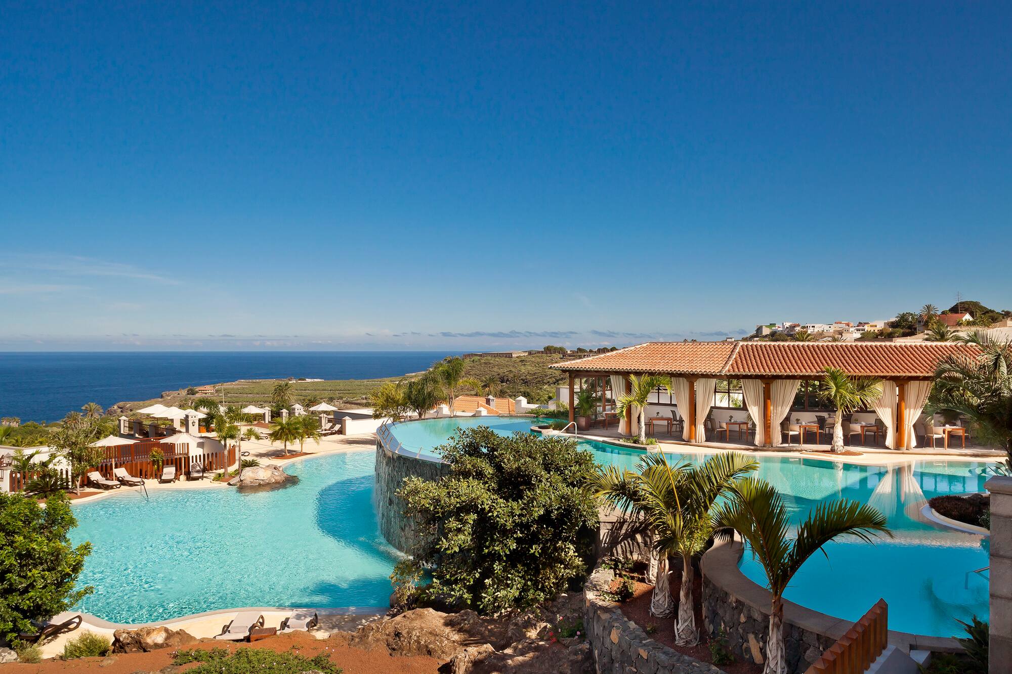 Tropical luxury resort with ocean view infinity pools, palm trees, and dining.
