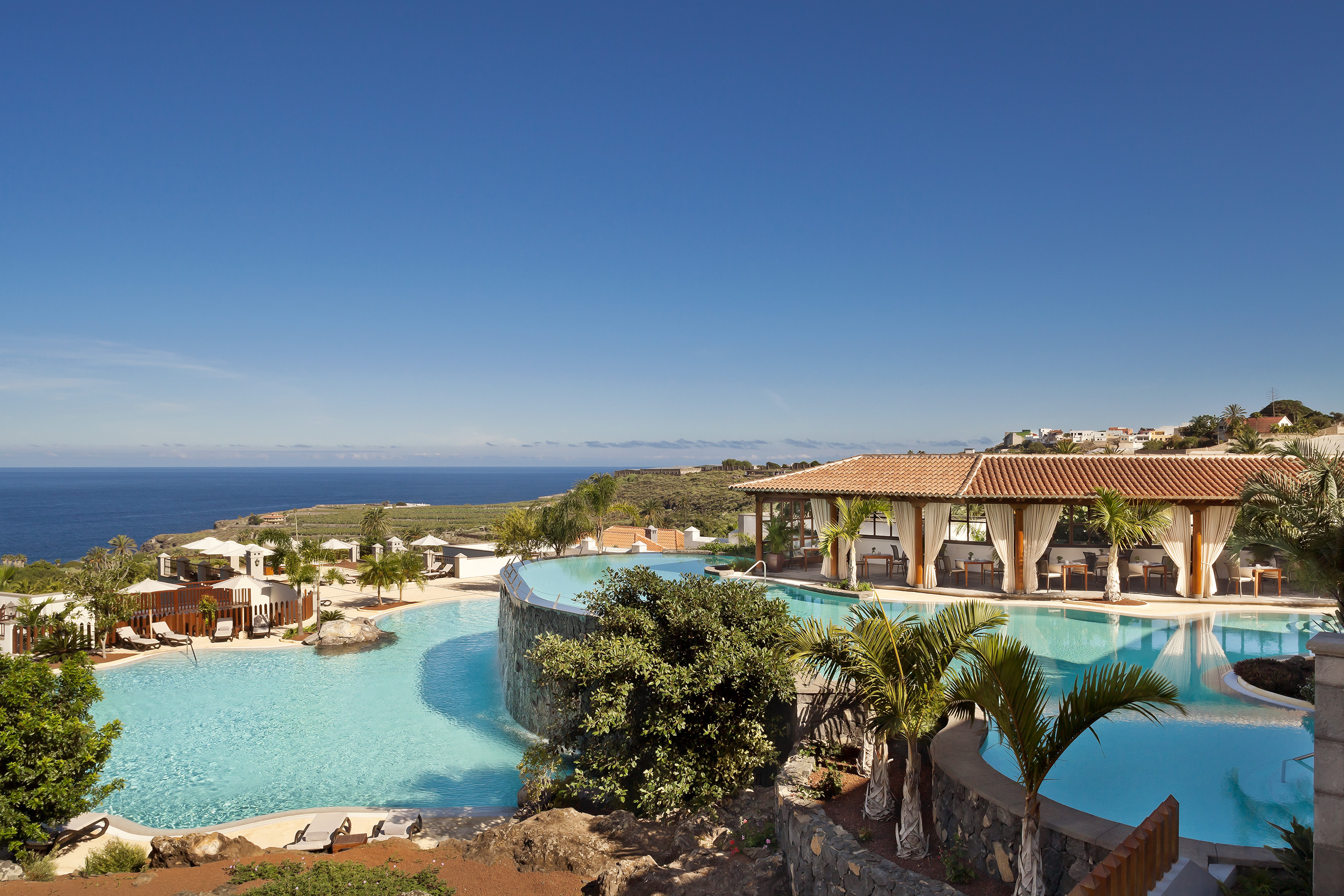 Tropical luxury resort with ocean view infinity pools, palm trees, and dining.