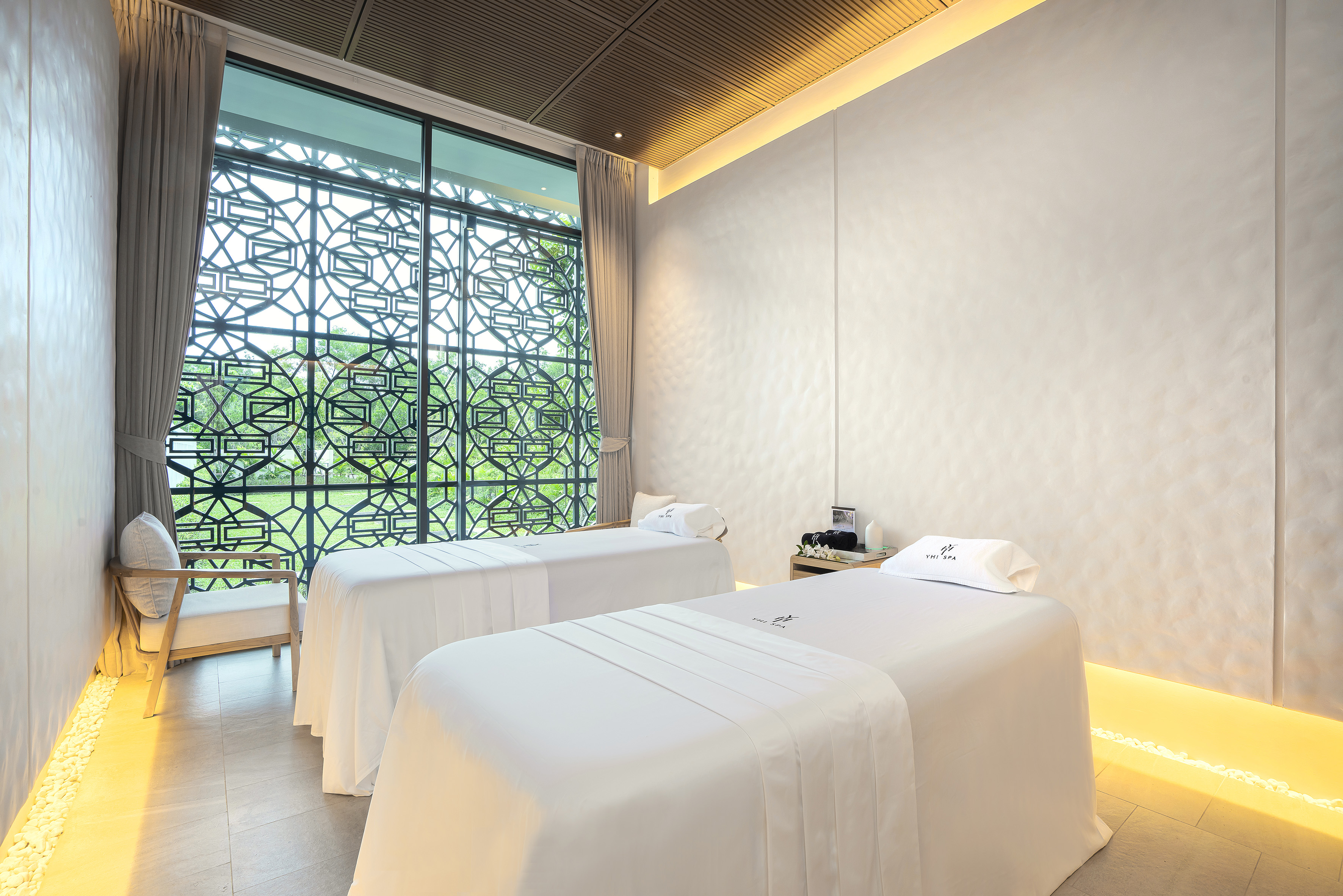 Luxury spa treatment room with two massage beds and decorative window.