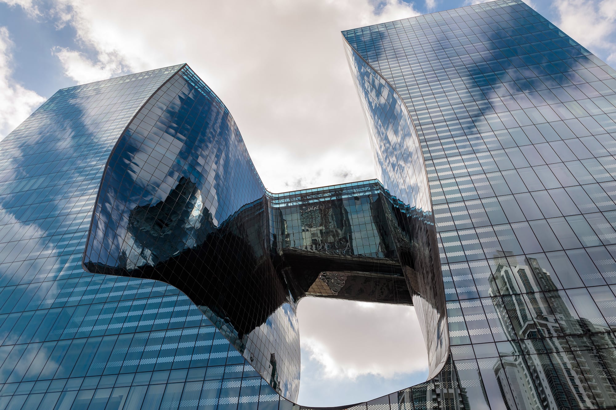 Modern glass skyscrapers connected by skybridges, reflecting clouds.