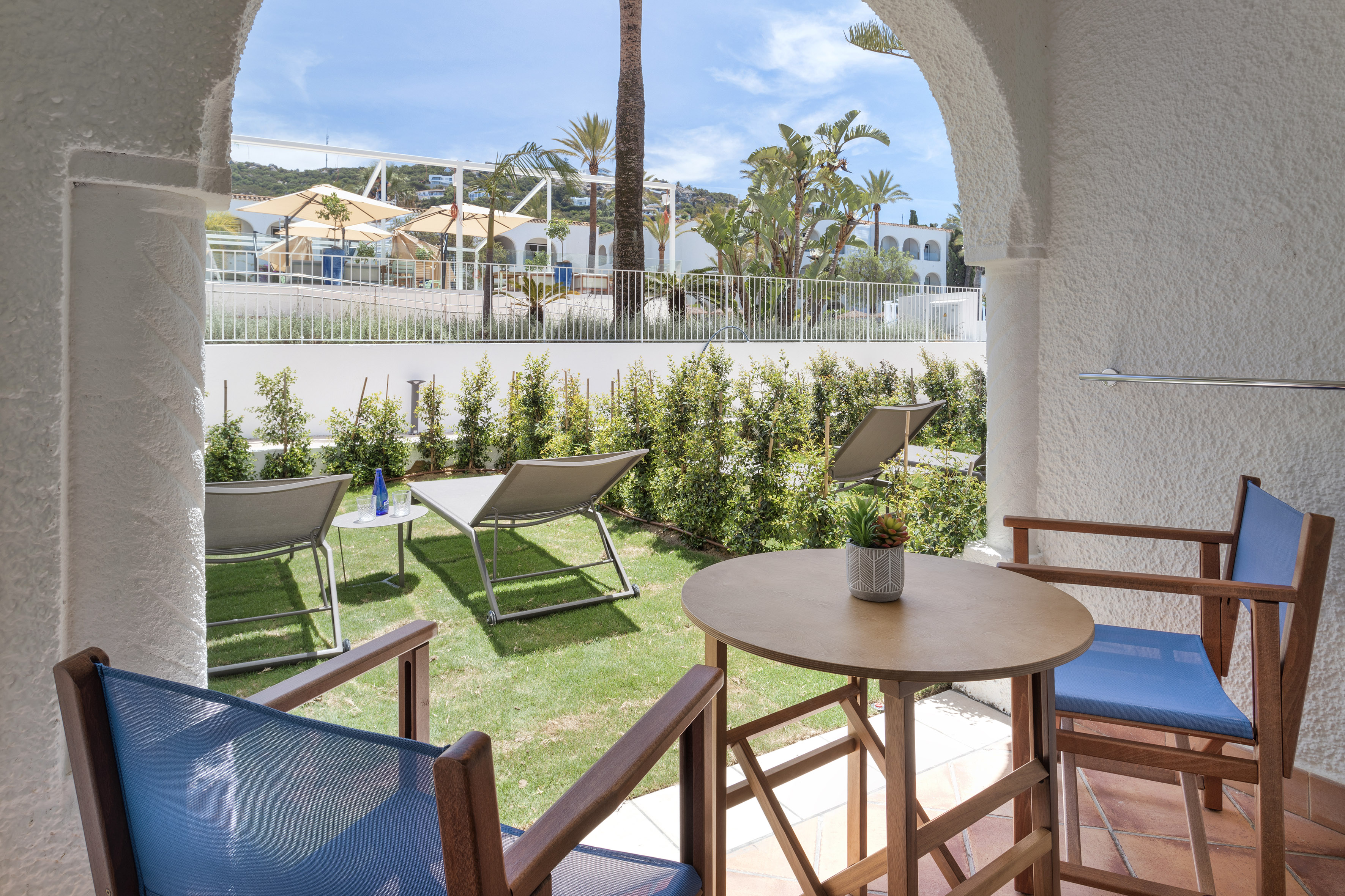Hotel patio with private garden, blue chairs, sun loungers, and resort view.