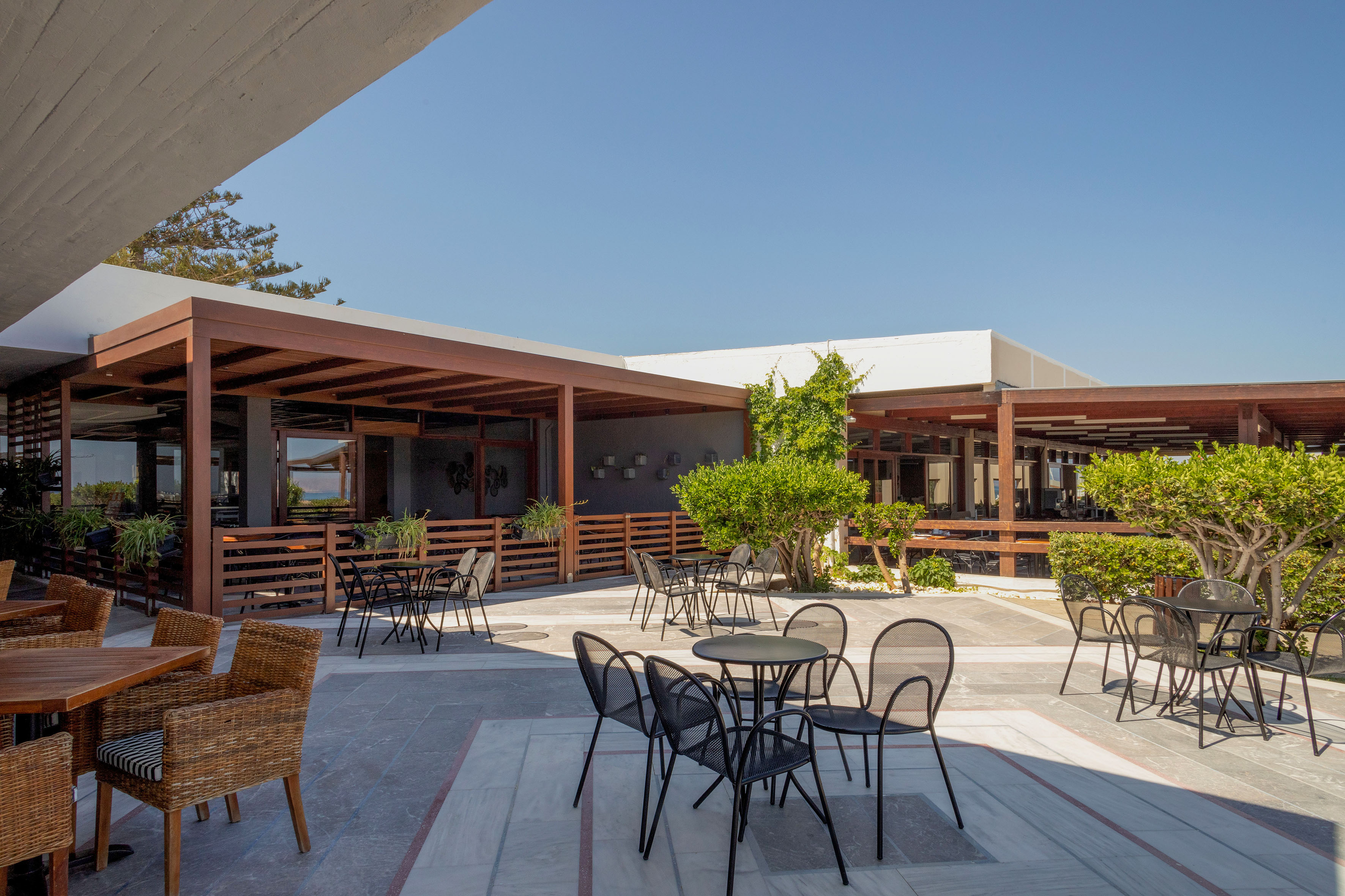 Modern outdoor patio with wooden pergolas, tables, chairs, and lush greenery.