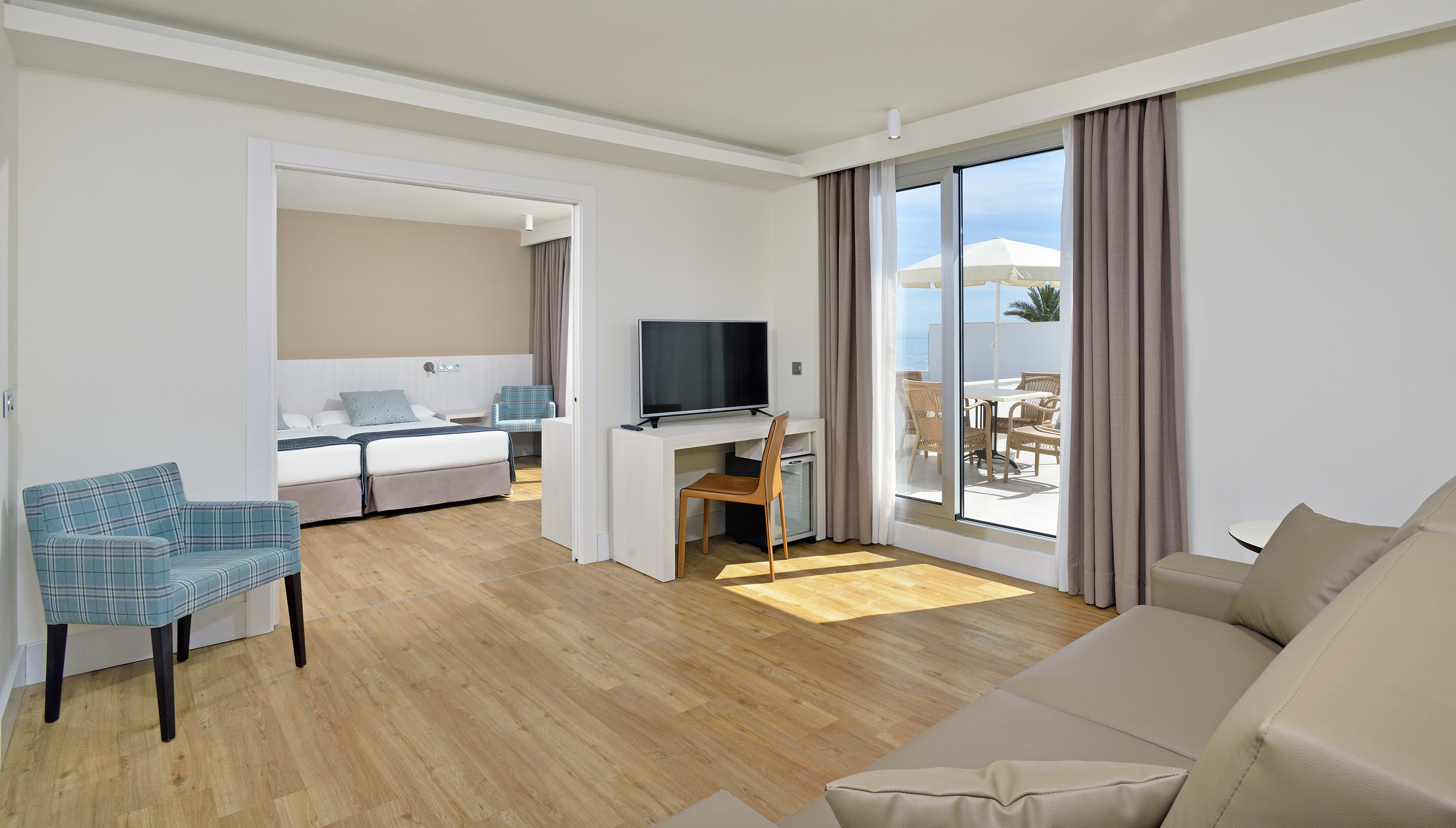 Modern hotel suite with living area, bedroom, and balcony with sea view.