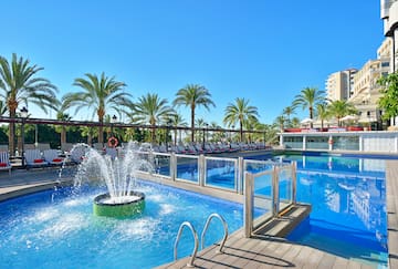 a pool with a fountain and a deck with chairs and a building