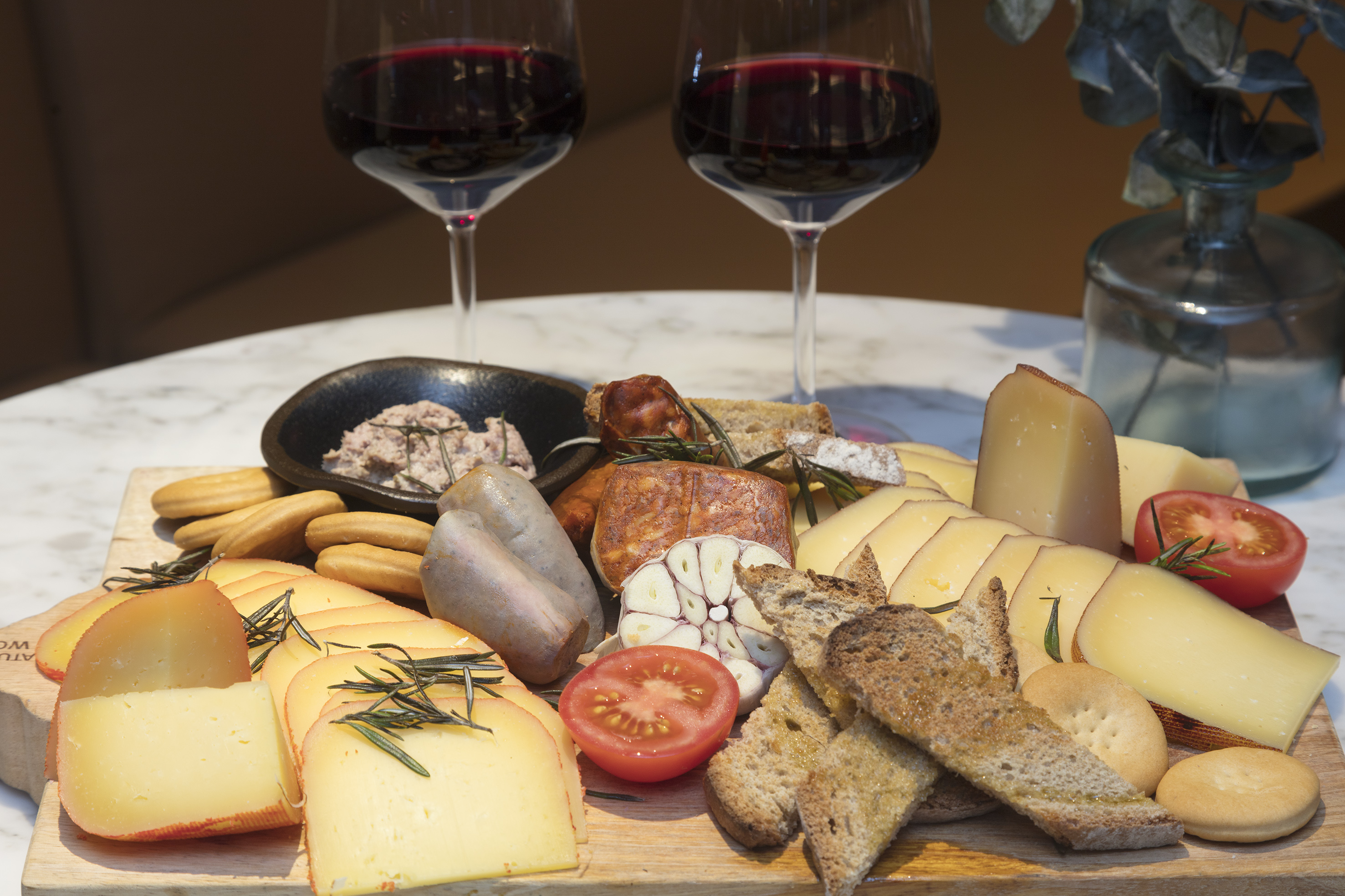 Gourmet cheese and charcuterie board with red wine, rosemary, and crackers.