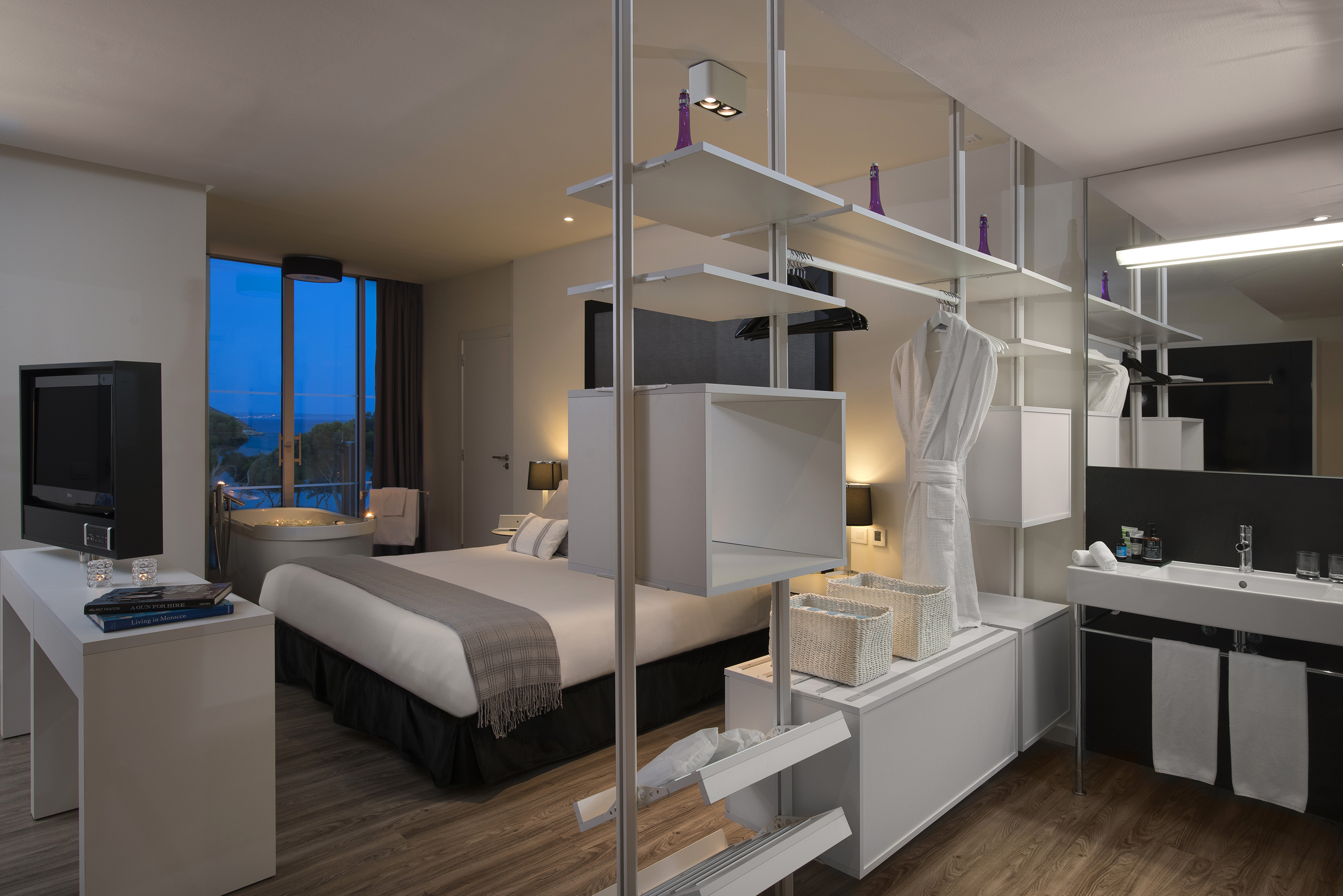 Stylish hotel bedroom with sea view, modern bed, bathtub, and open wardrobe.
