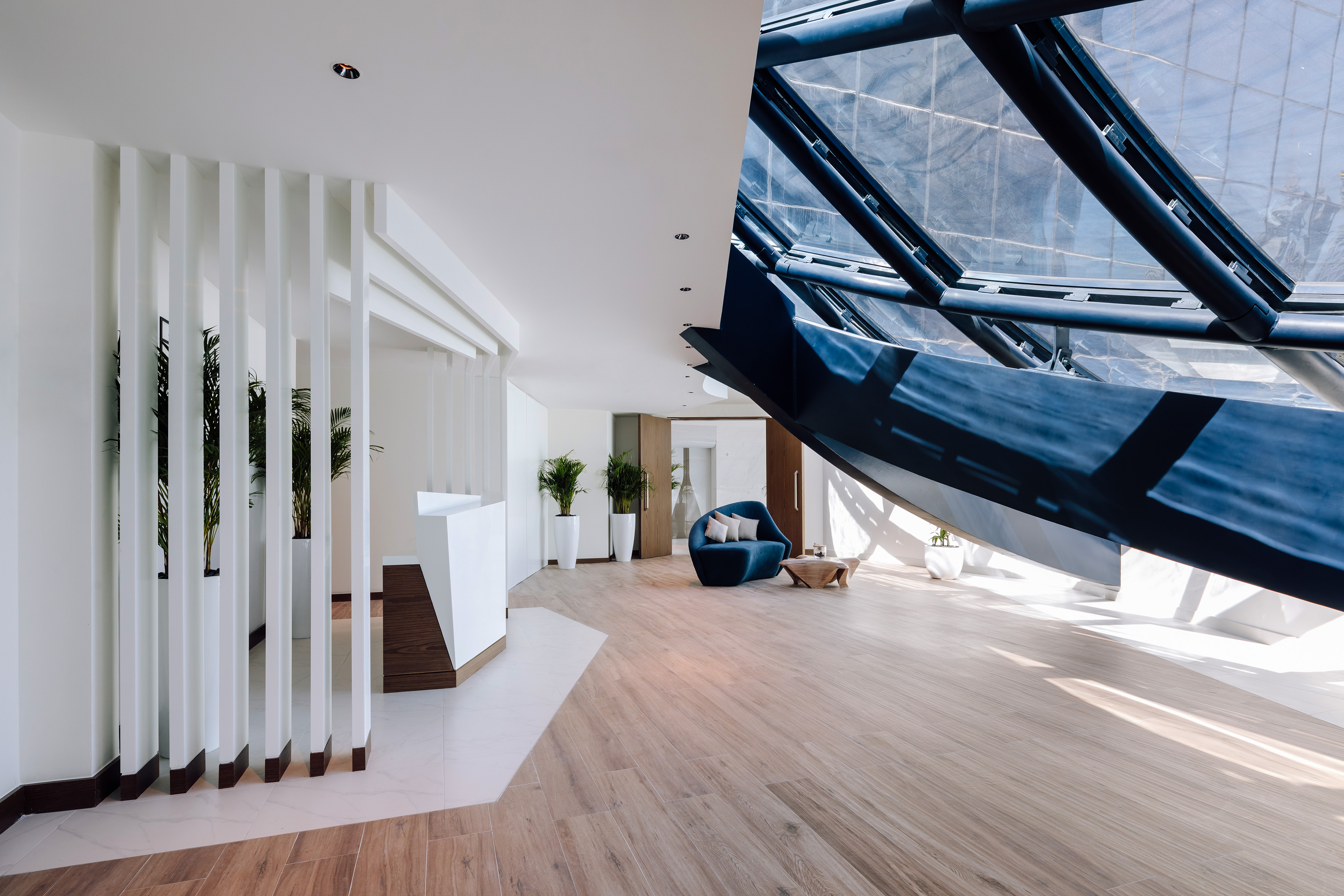 Modern reception lobby with curved blue sofa, wood floor, and large glass skylight.