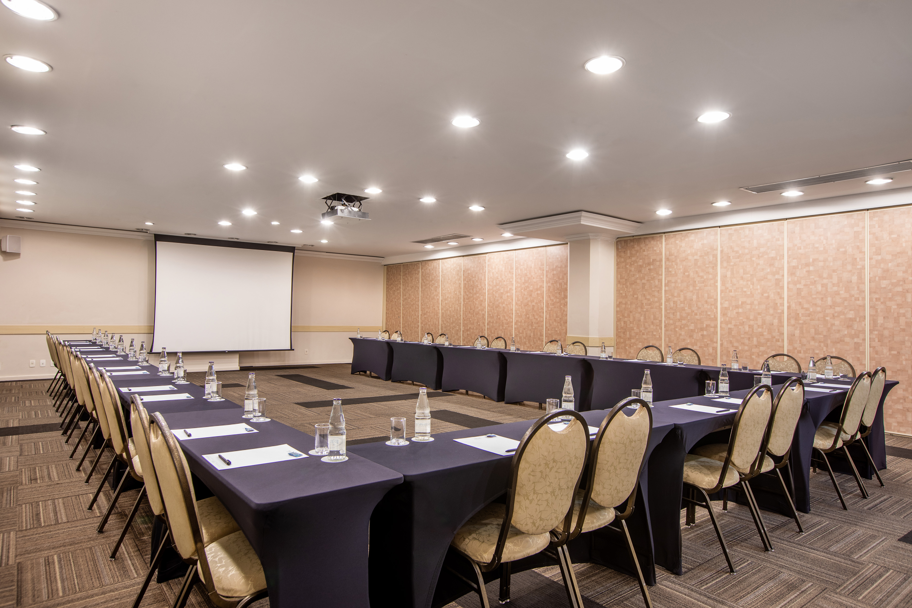 U-shaped meeting room setup with projector screen, dark tables, and chairs.