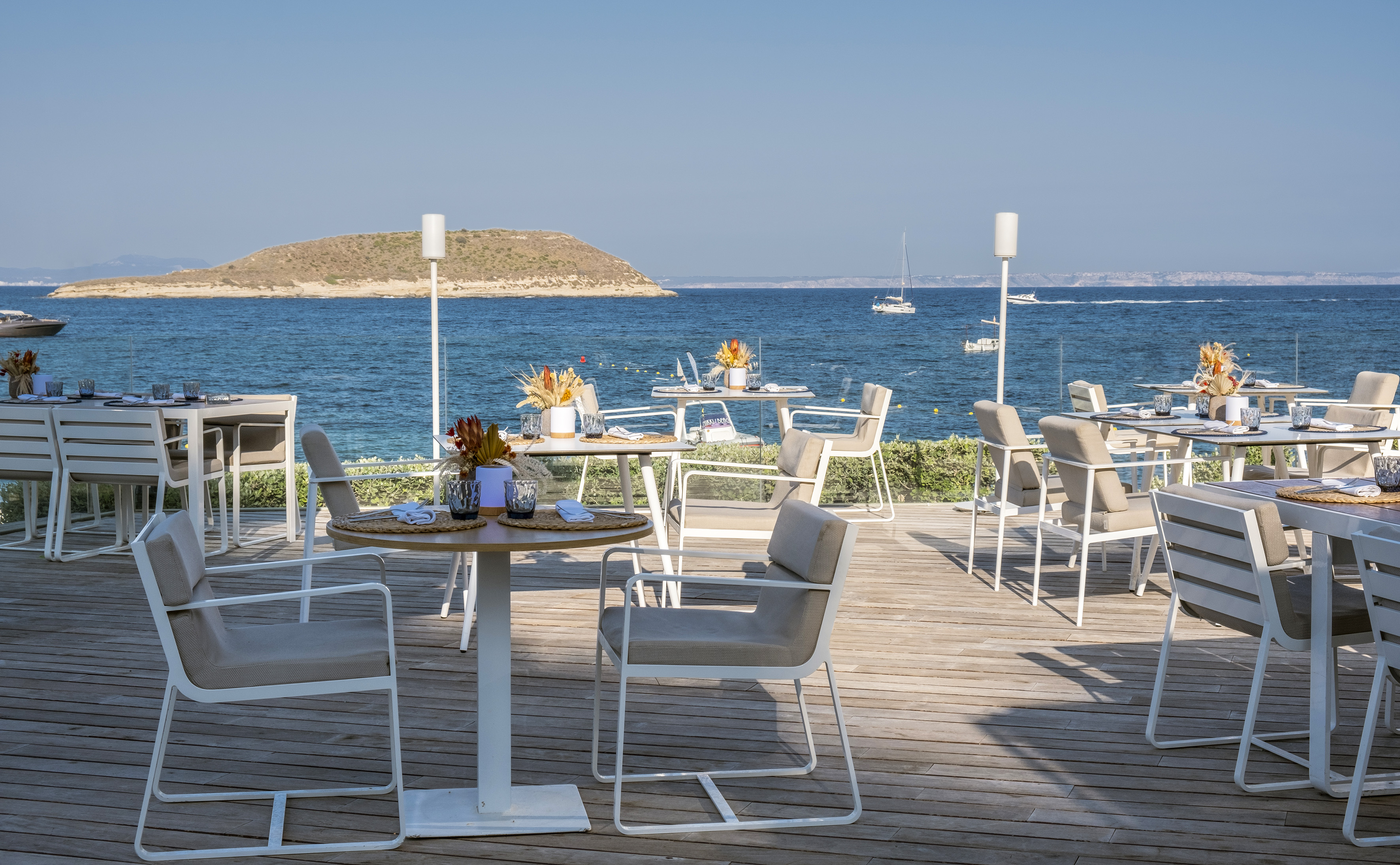 Modern outdoor dining patio with sea view, tables, chairs, and island.