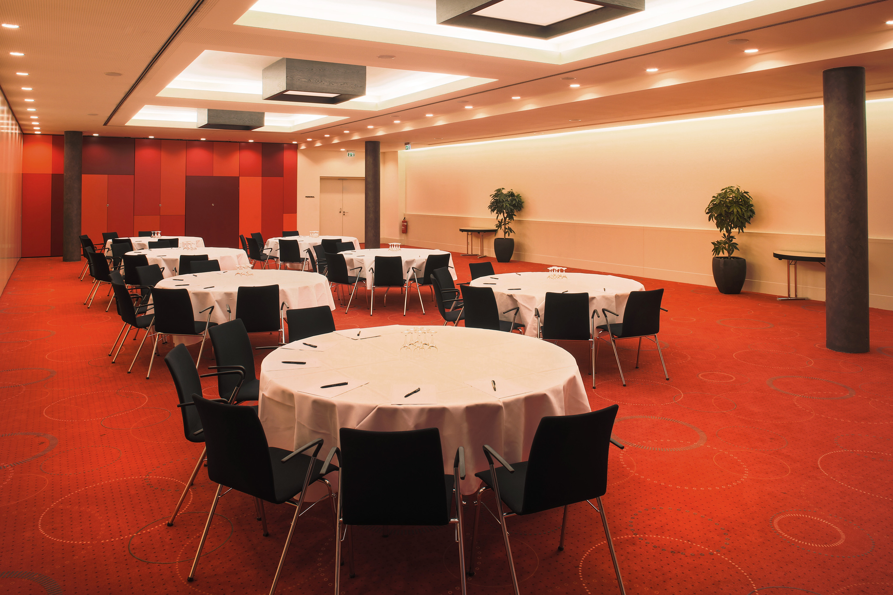 Modern meeting room setup with round tables, black chairs, and red carpet.