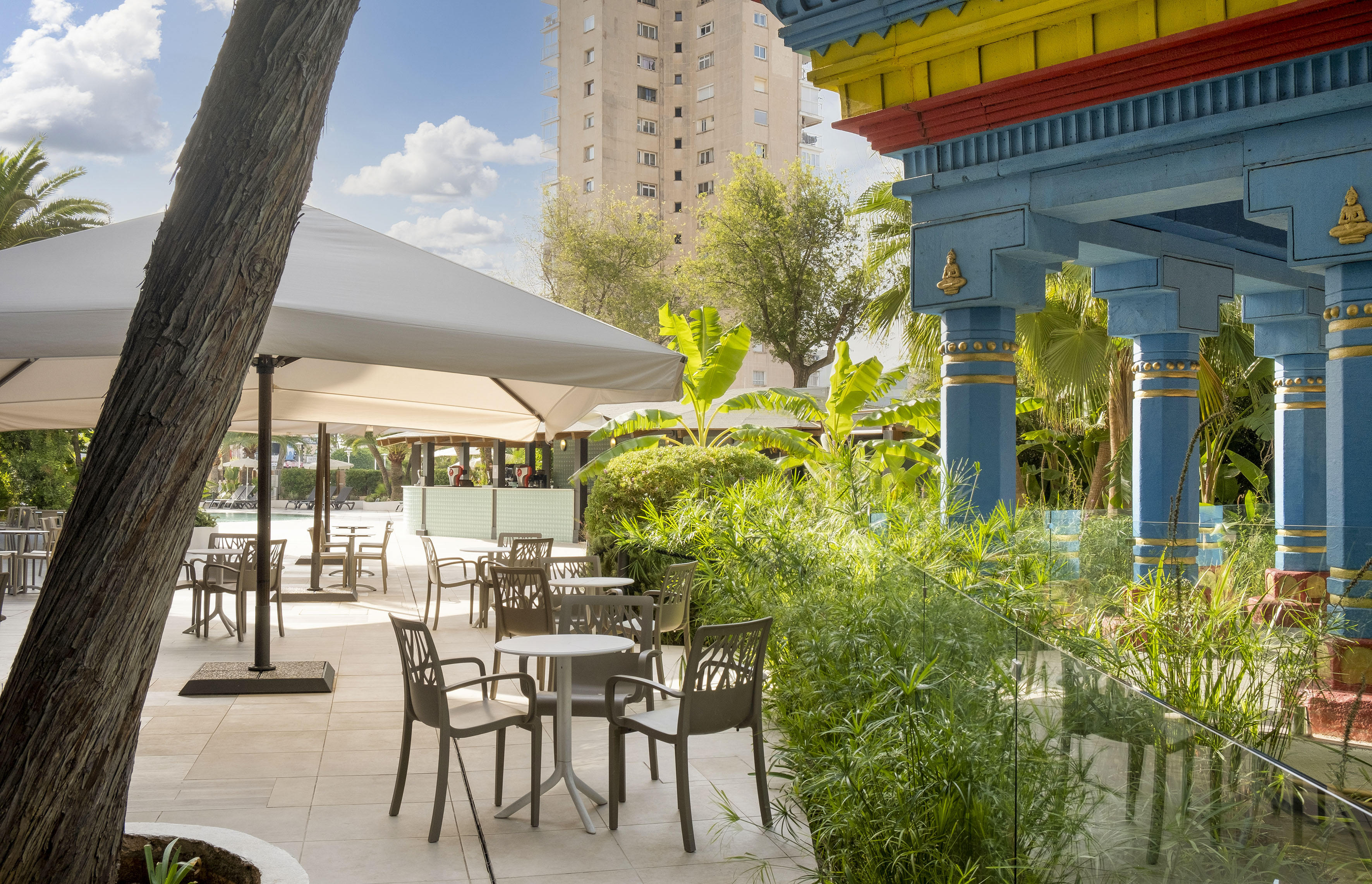 Outdoor resort patio with al fresco dining, lush tropical plants, and ornate columns.