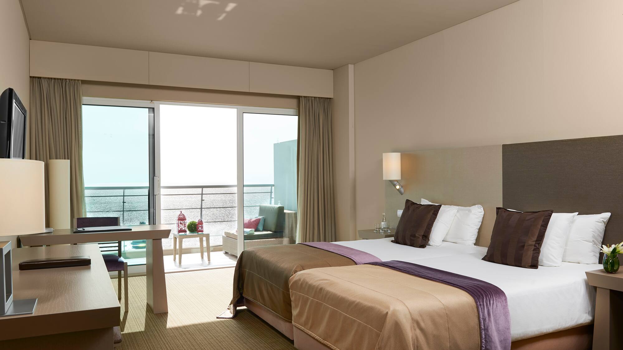 Modern hotel room with twin beds, desk, and ocean view balcony.