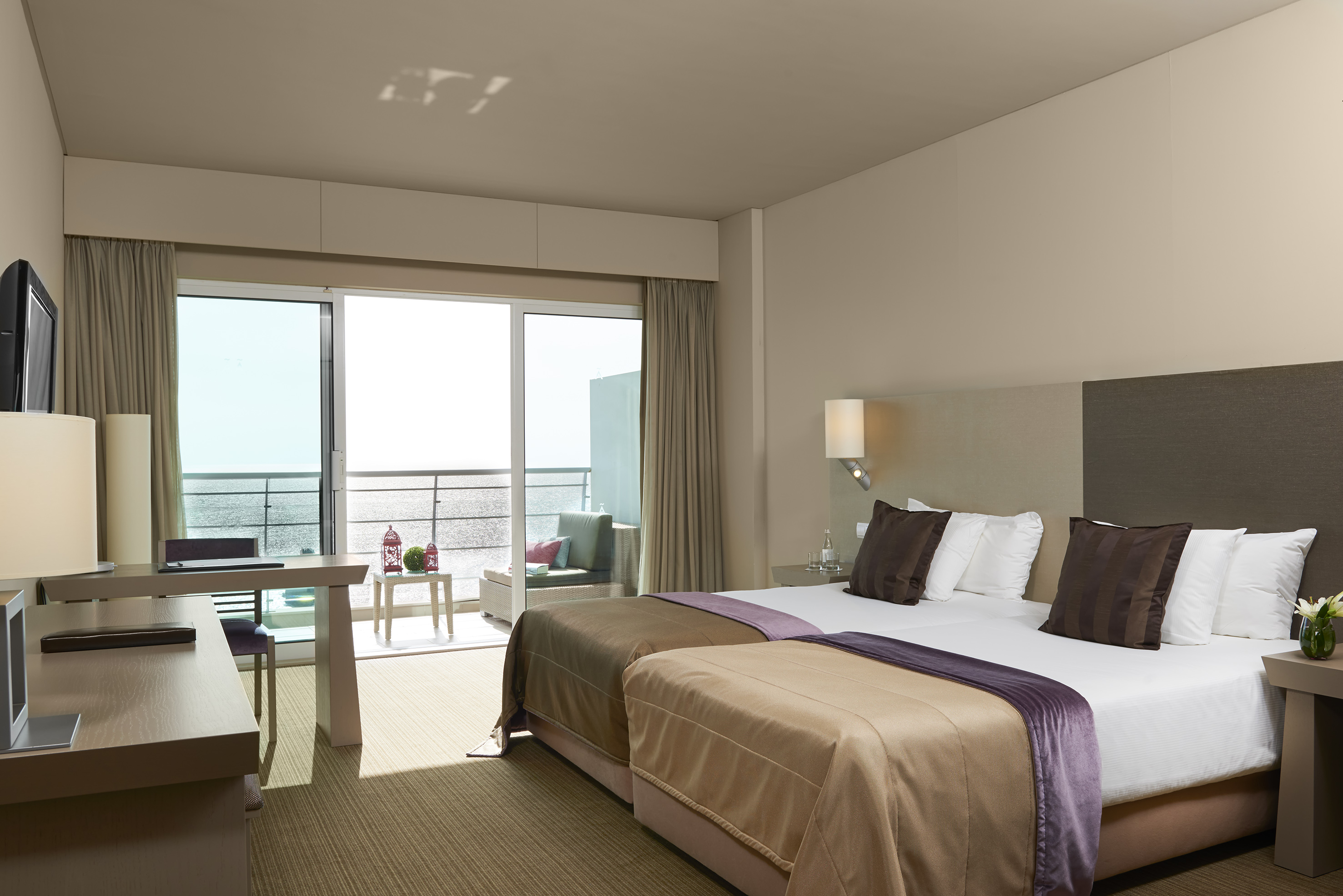 Modern hotel room with twin beds, desk, and ocean view balcony.