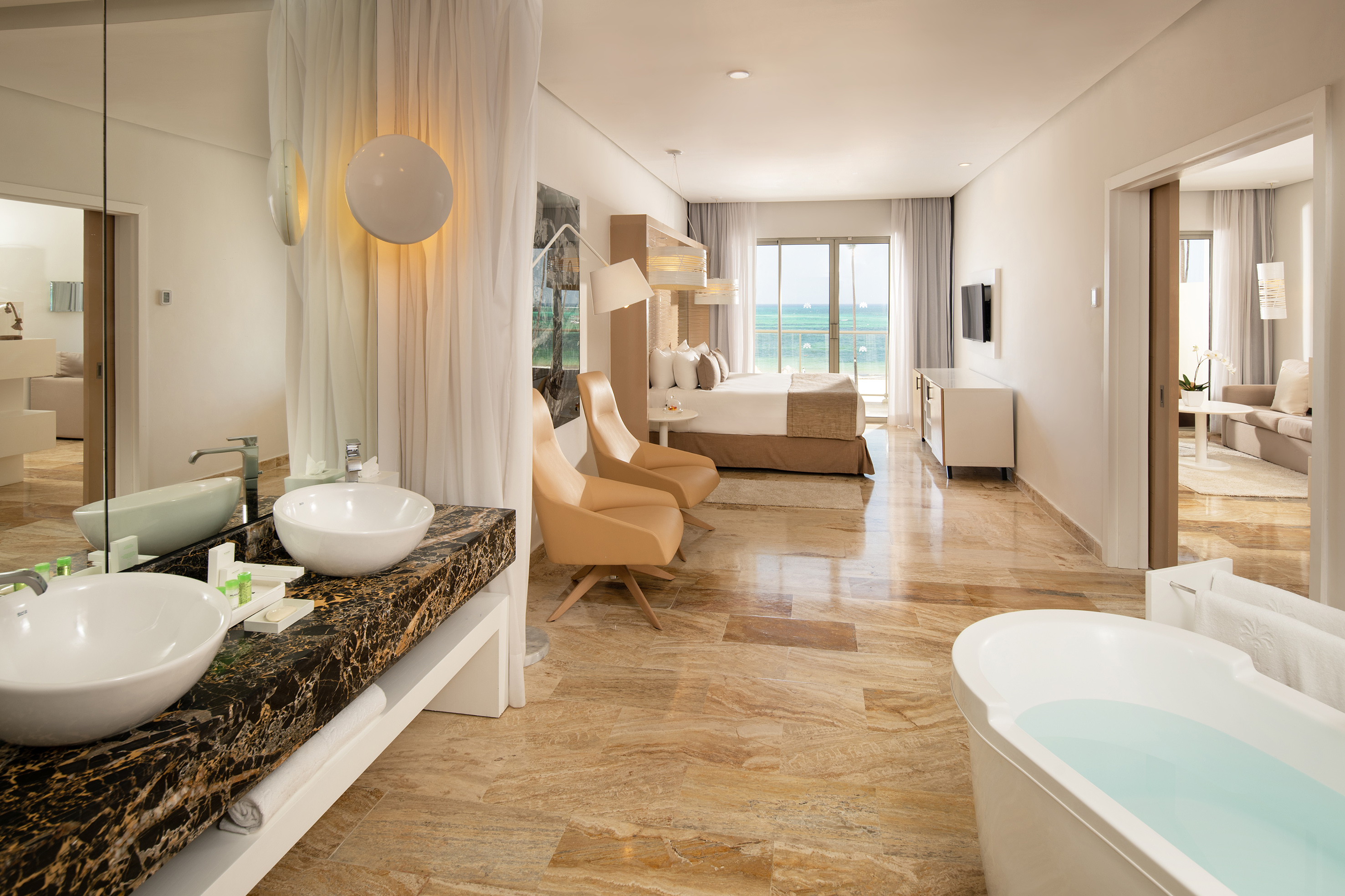Luxury ocean view hotel suite with bedroom, open bathroom, and soaking tub.
