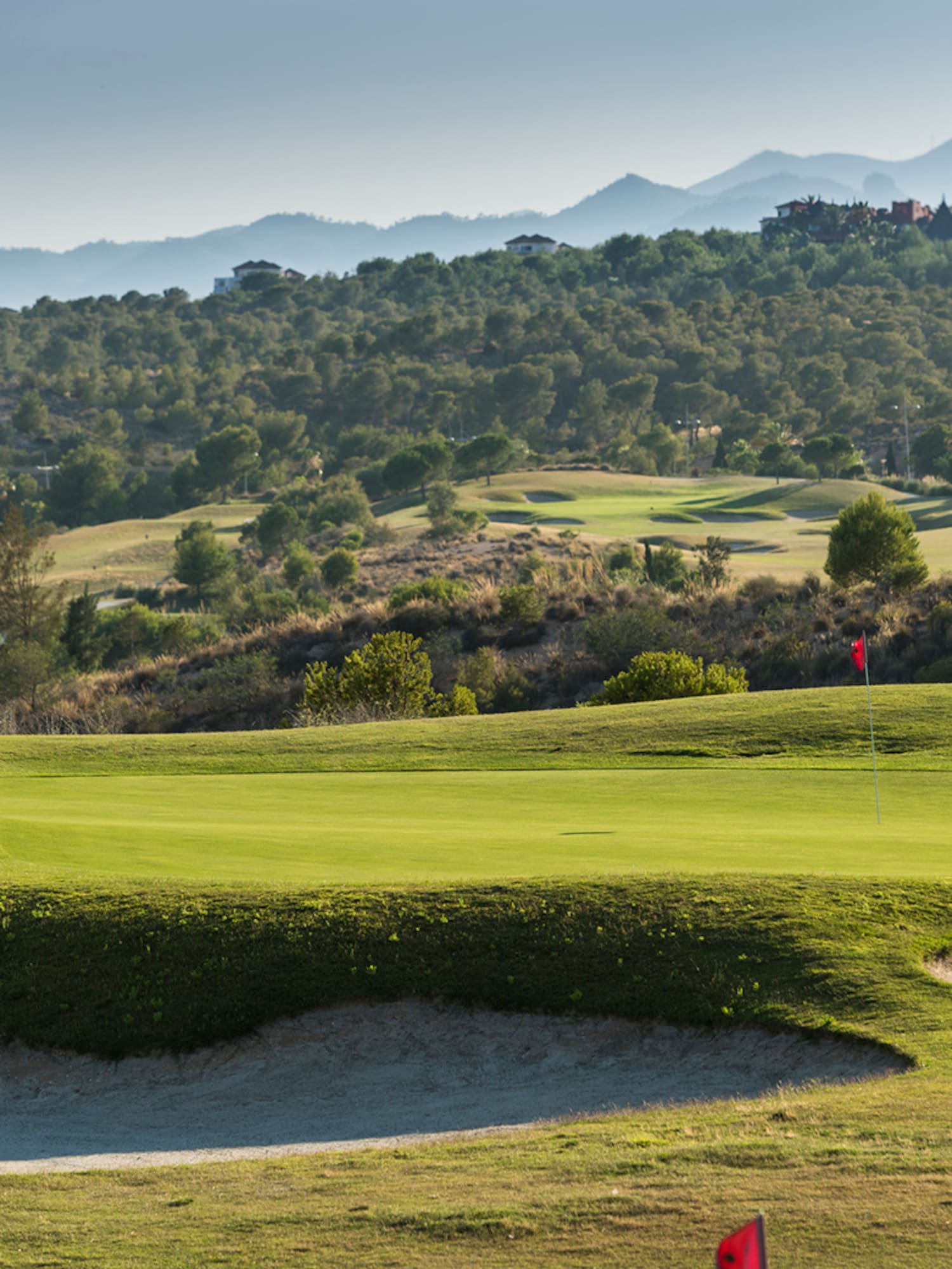 a golf course with sand bunkers and hills in the background