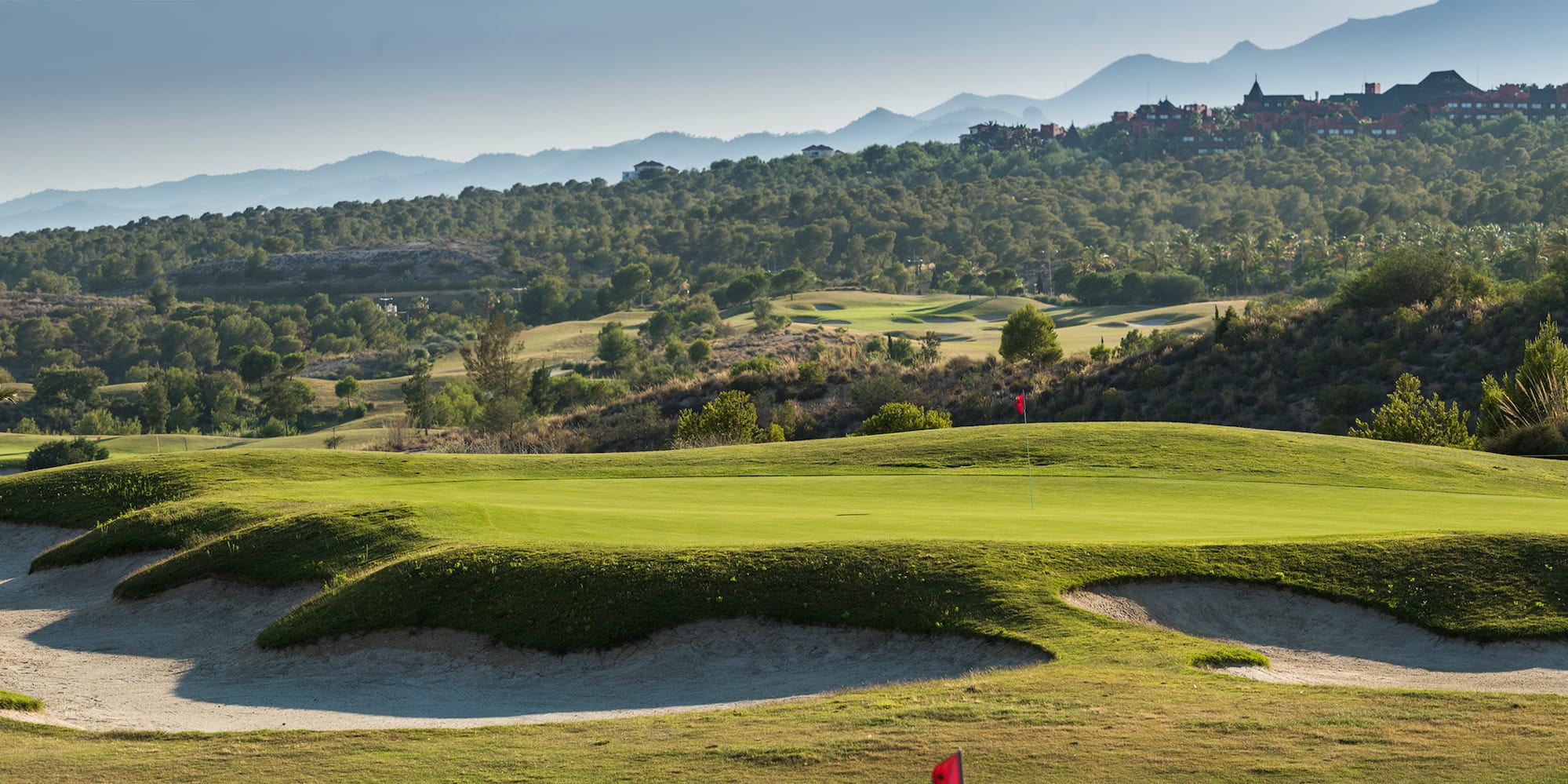 a golf course with sand bunkers and hills in the background