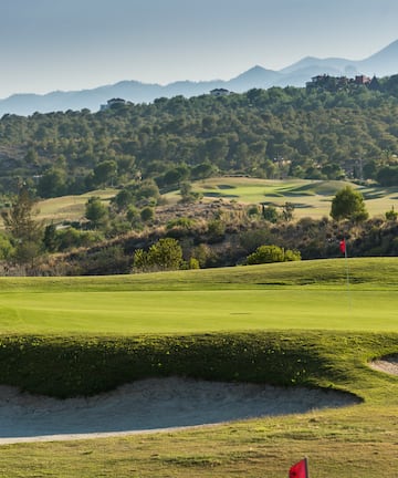 a golf course with sand bunkers and hills in the background