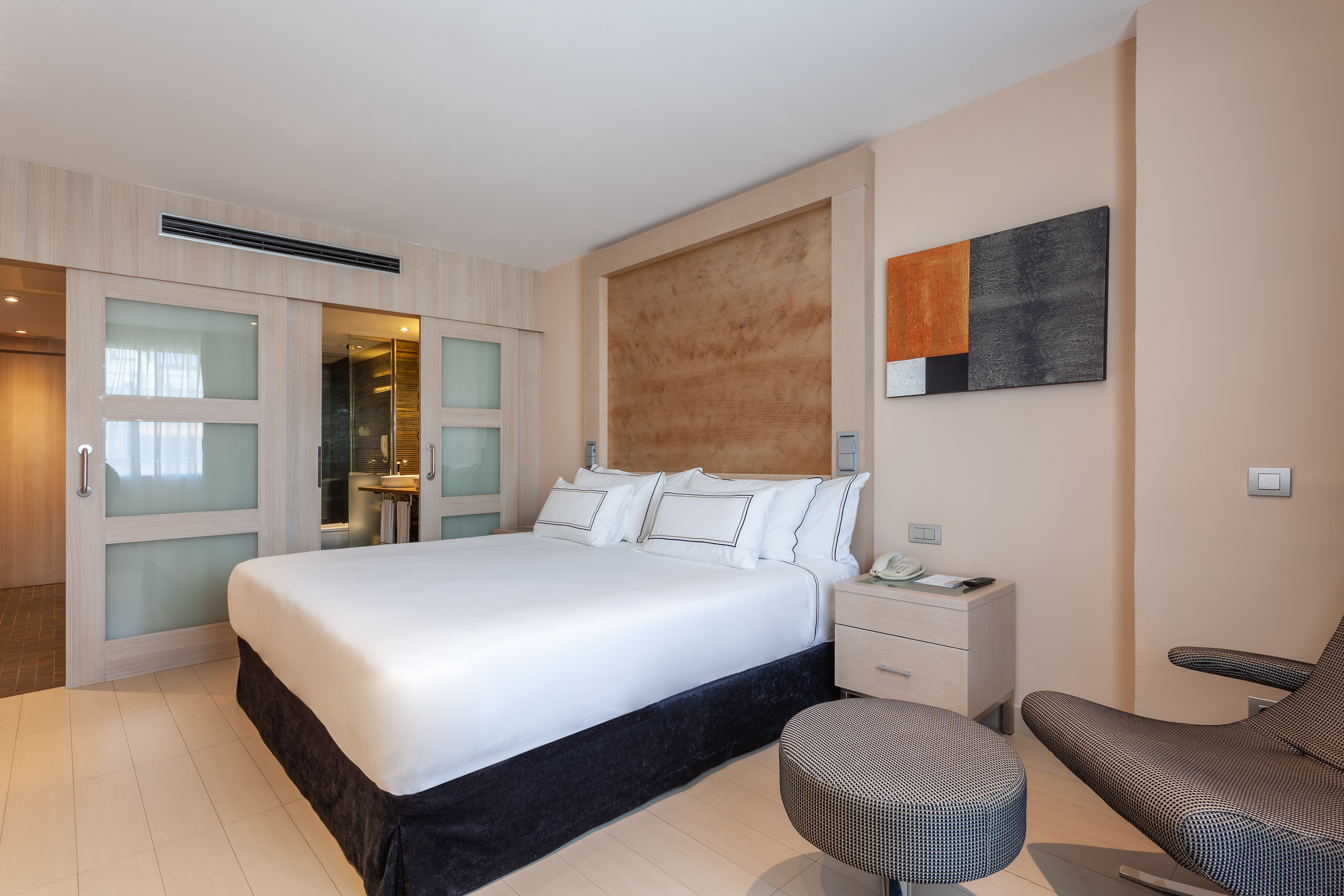 Modern hotel bedroom with king bed, abstract art, and sliding bathroom doors.