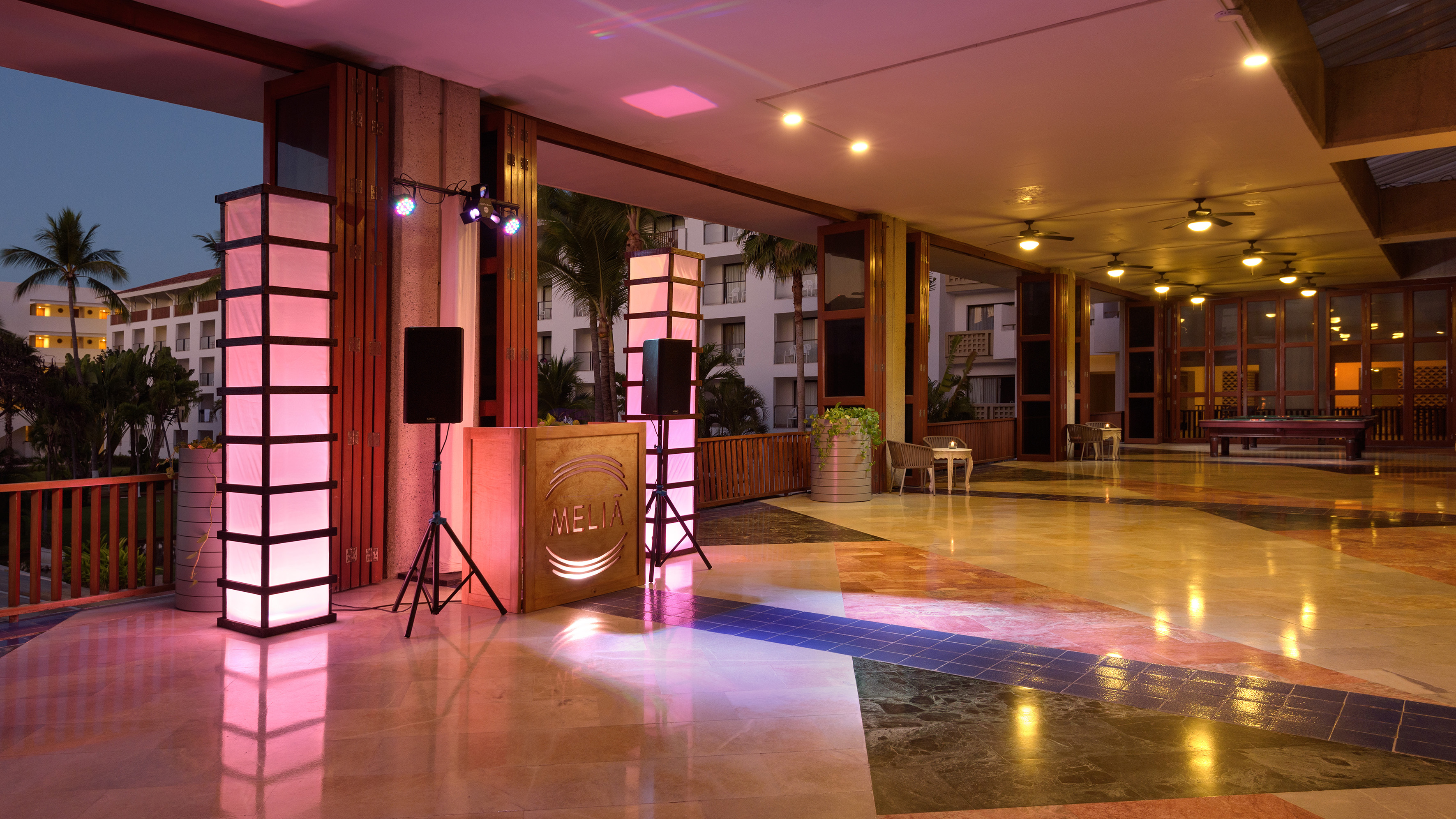 Meliá DJ booth with pink lighting in a vibrant resort lobby at dusk.
