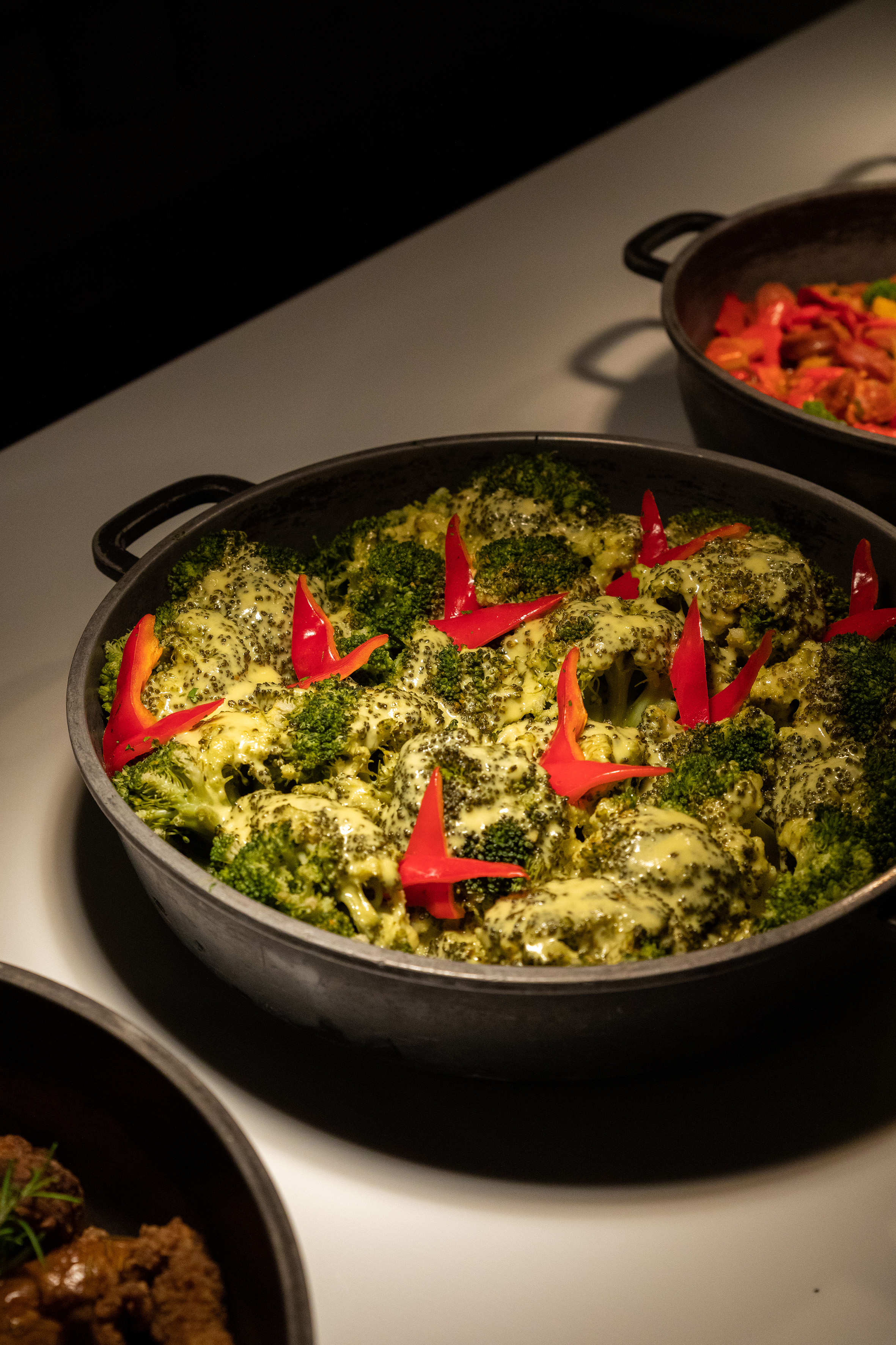 Creamy broccoli and red peppers in a large serving pan at a buffet.